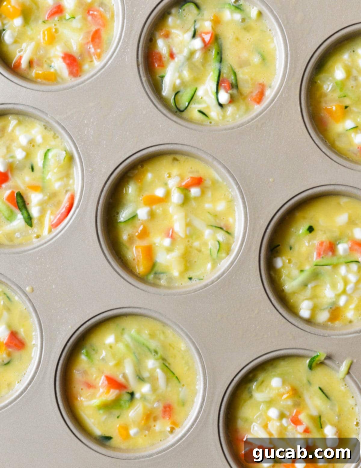 Unbaked egg muffin mixture evenly distributed across a 12-cup muffin tin, ready for the oven.