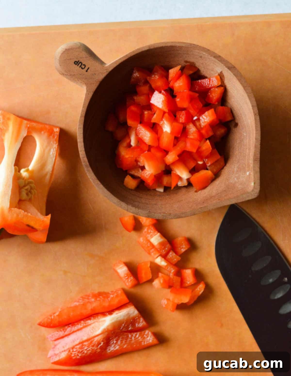Colorful diced bell pepper on a cutting board, with some transferred to a measuring cup, indicating small, uniform cuts.