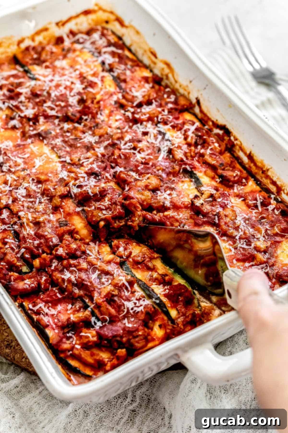 hand using a metal spatula to cut a zucchini lasagna. 