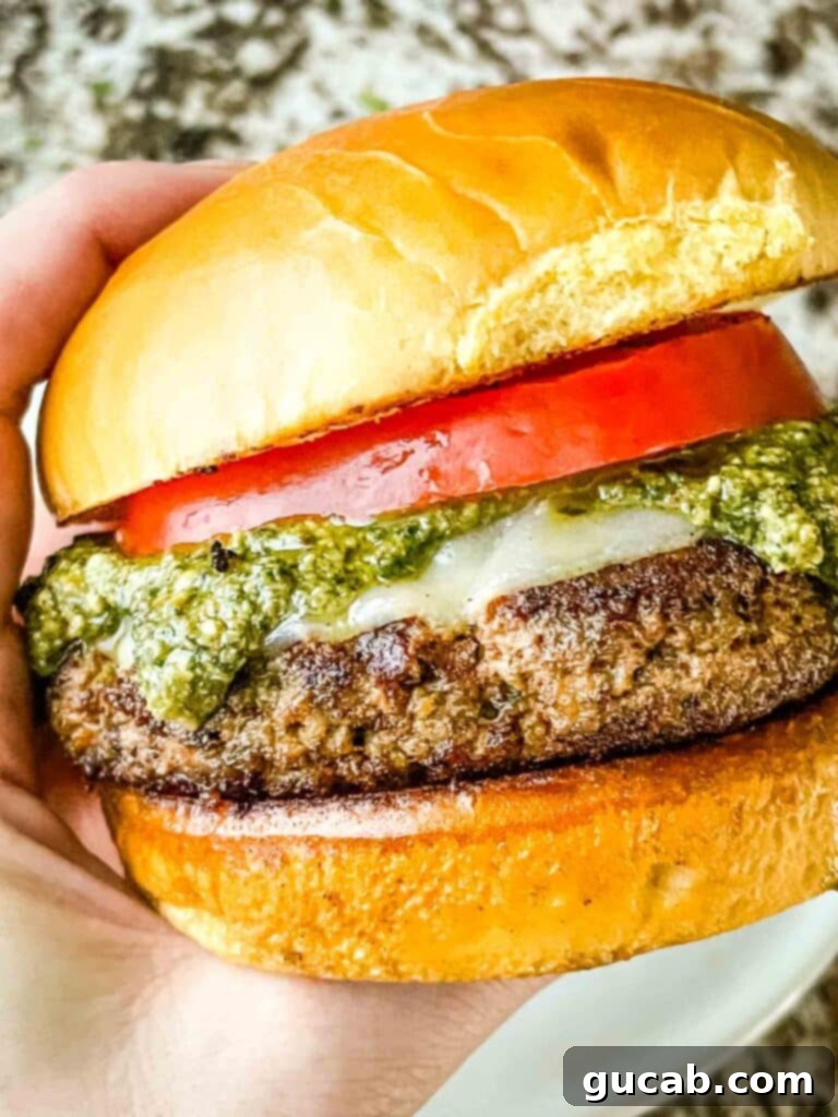 hand holding a turkey burger with sliced tomato, pesto, and cheese on it. 