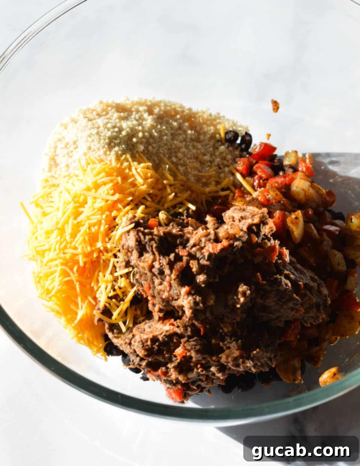 A bowl containing a delicious mixture of shredded cheese, plain bread crumbs, and the prepared black bean and red pepper paste, all ready to be combined for forming the black bean burger patties.