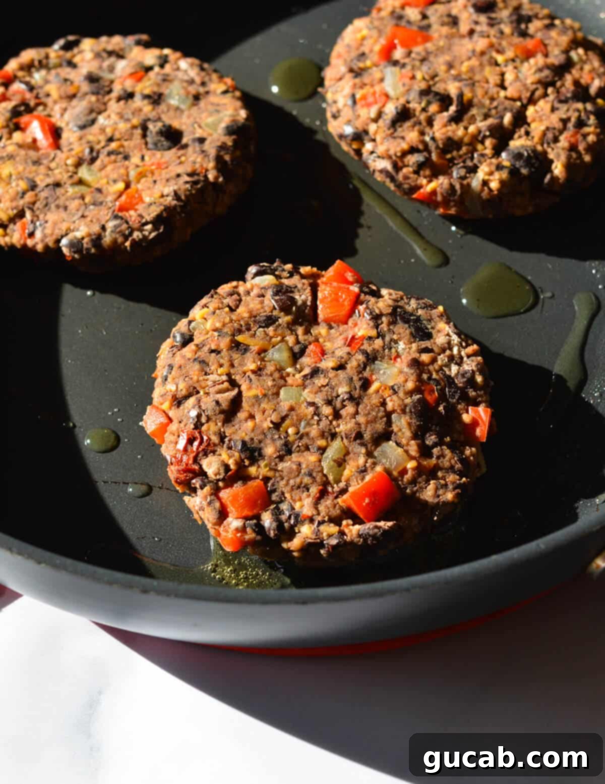 Black bean patties sizzling in a hot nonstick skillet with olive oil, developing a delicious golden-brown crust and cooking through evenly.