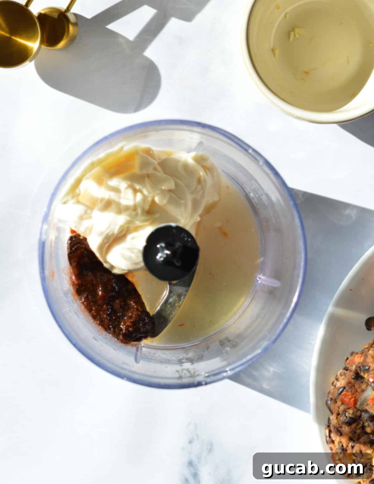 All the fresh ingredients for creamy chipotle mayo, including mayonnaise, a chipotle pepper in adobo, fresh lime juice, and a touch of honey, neatly placed in a food processor ready to blend into a smooth sauce.