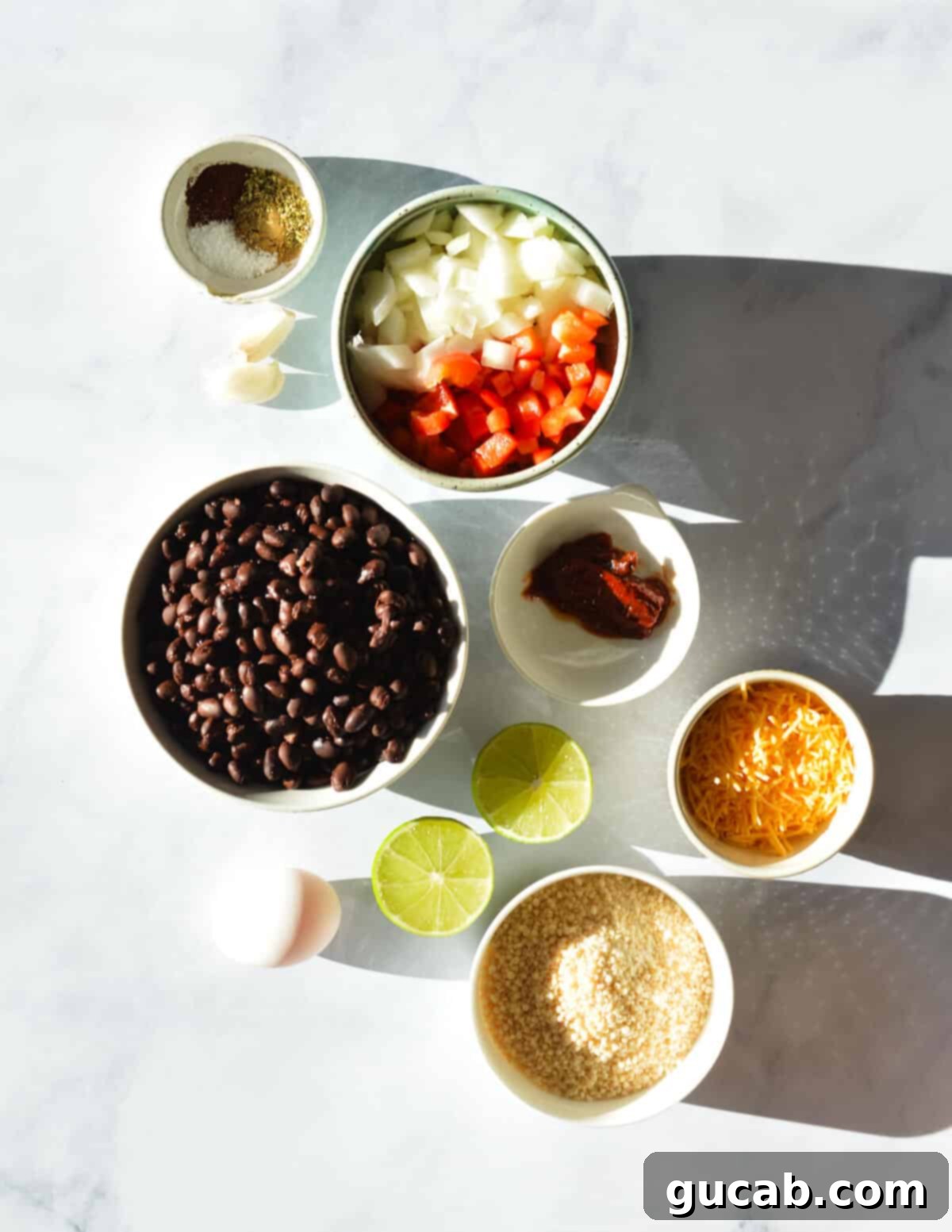 A vibrant flat lay showcasing all the fresh and dry key ingredients needed for delicious chipotle black bean burgers: rinsed black beans, a selection of spices (cumin, oregano, chili powder, salt), diced bell peppers and onions, a whole chipotle pepper in adobo sauce, a fresh lime, shredded cheddar cheese, and plain bread crumbs.