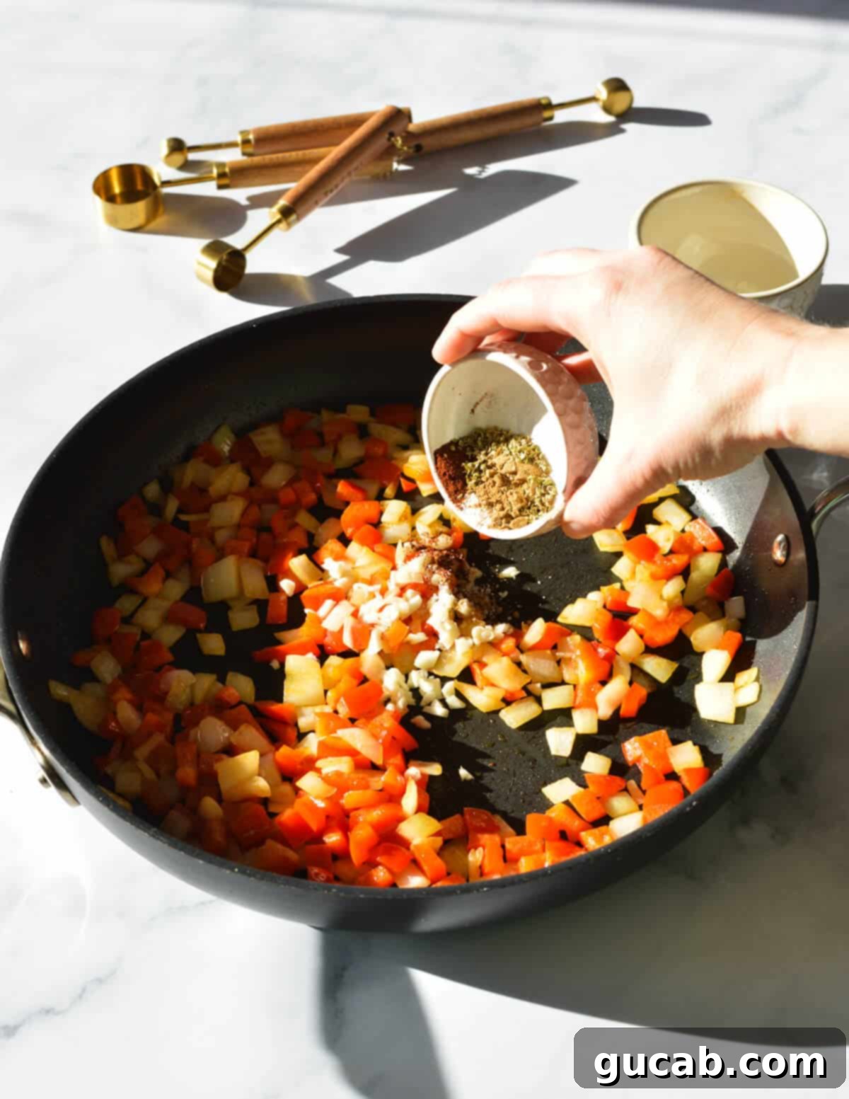 A hand carefully adding a blend of savory spices, including cumin, oregano, and chili powder, to the sautéing peppers and onions in a skillet, to infuse rich flavor into the black bean burgers.