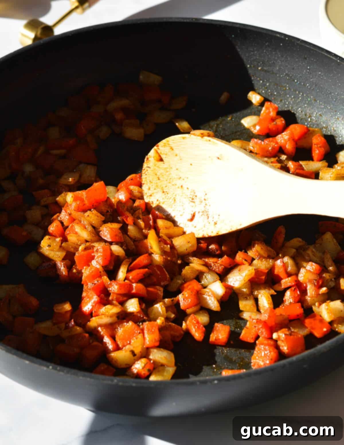 A wooden spoon actively stirring fragrant sautéed onions, bell peppers, and spices in a skillet, creating a rich and aromatic base that will form the heart of the black bean burgers.