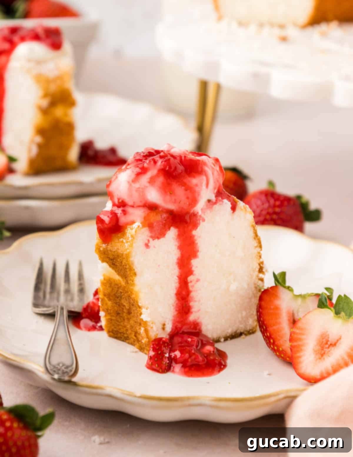 A perfectly sliced piece of angel food cake, topped with fresh whipped cream and a luscious strawberry sauce.