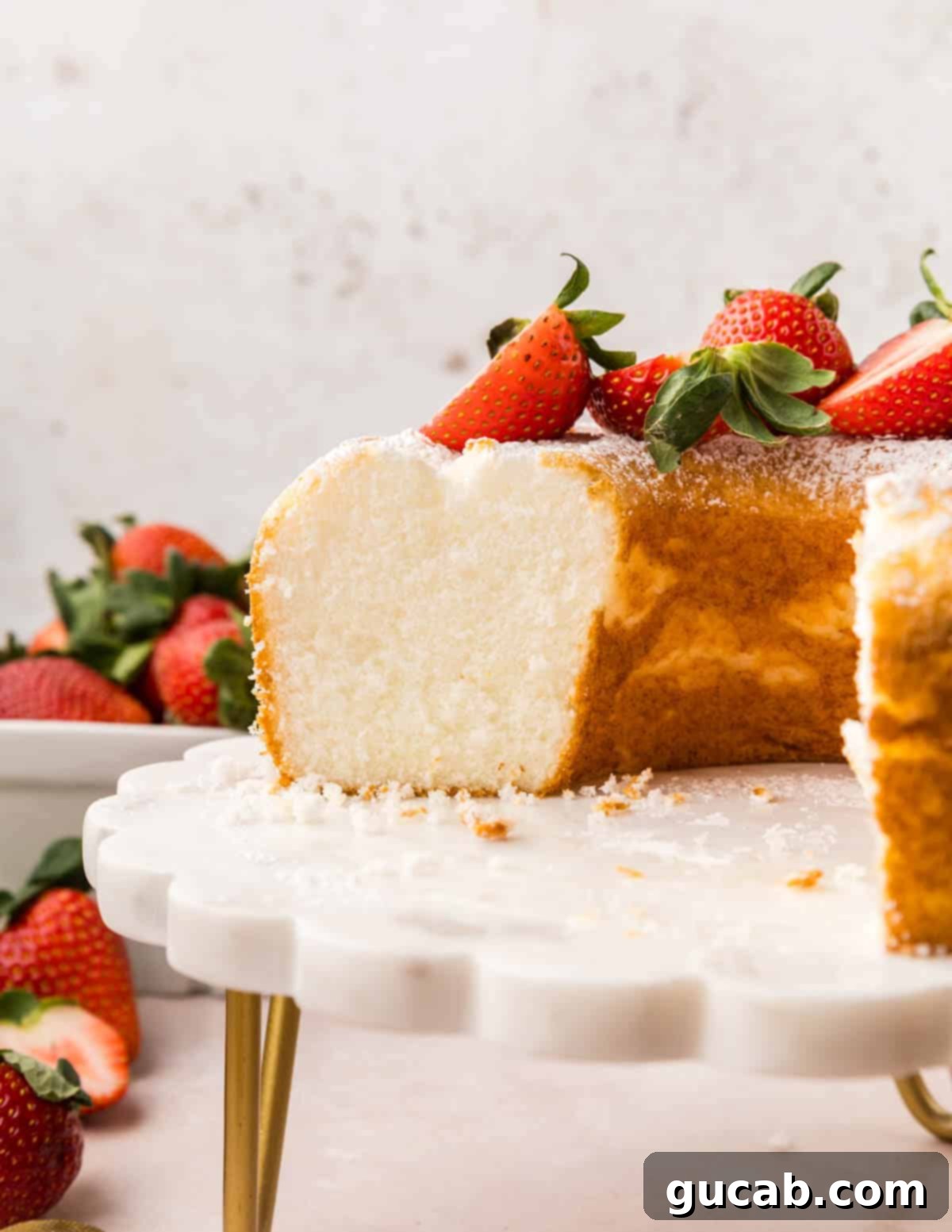 A slice of angel food cake, showing its airy texture, with fresh strawberries piled on top.