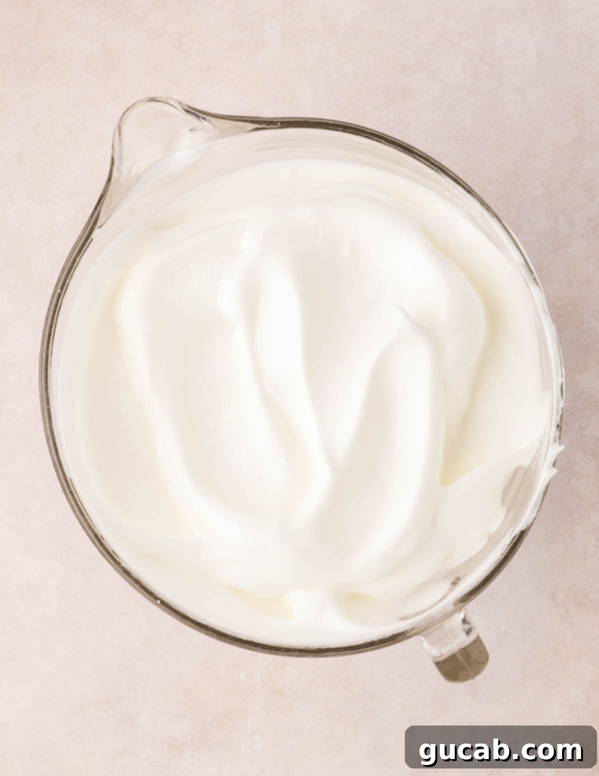 Perfectly whipped egg whites in a mixing bowl, showing stiff peaks formed by the whisk.