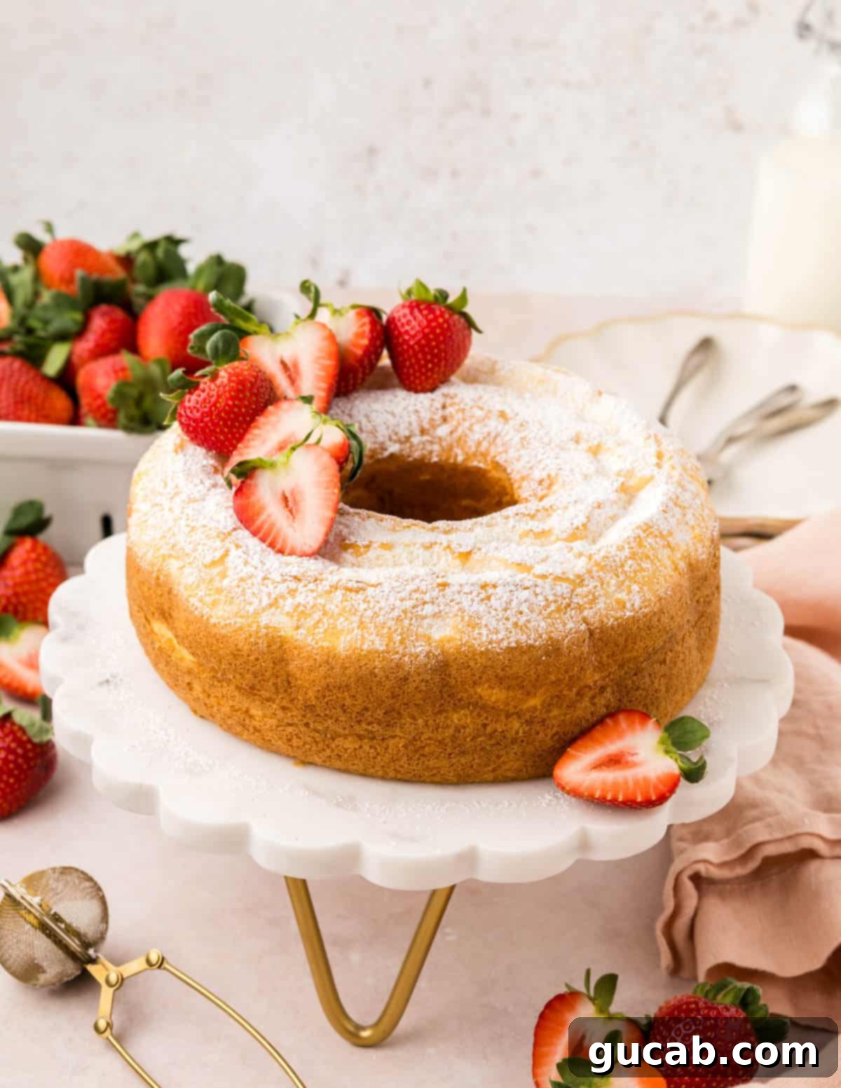 Baked angel food cake beautifully presented on a cake stand, garnished with fresh strawberries.