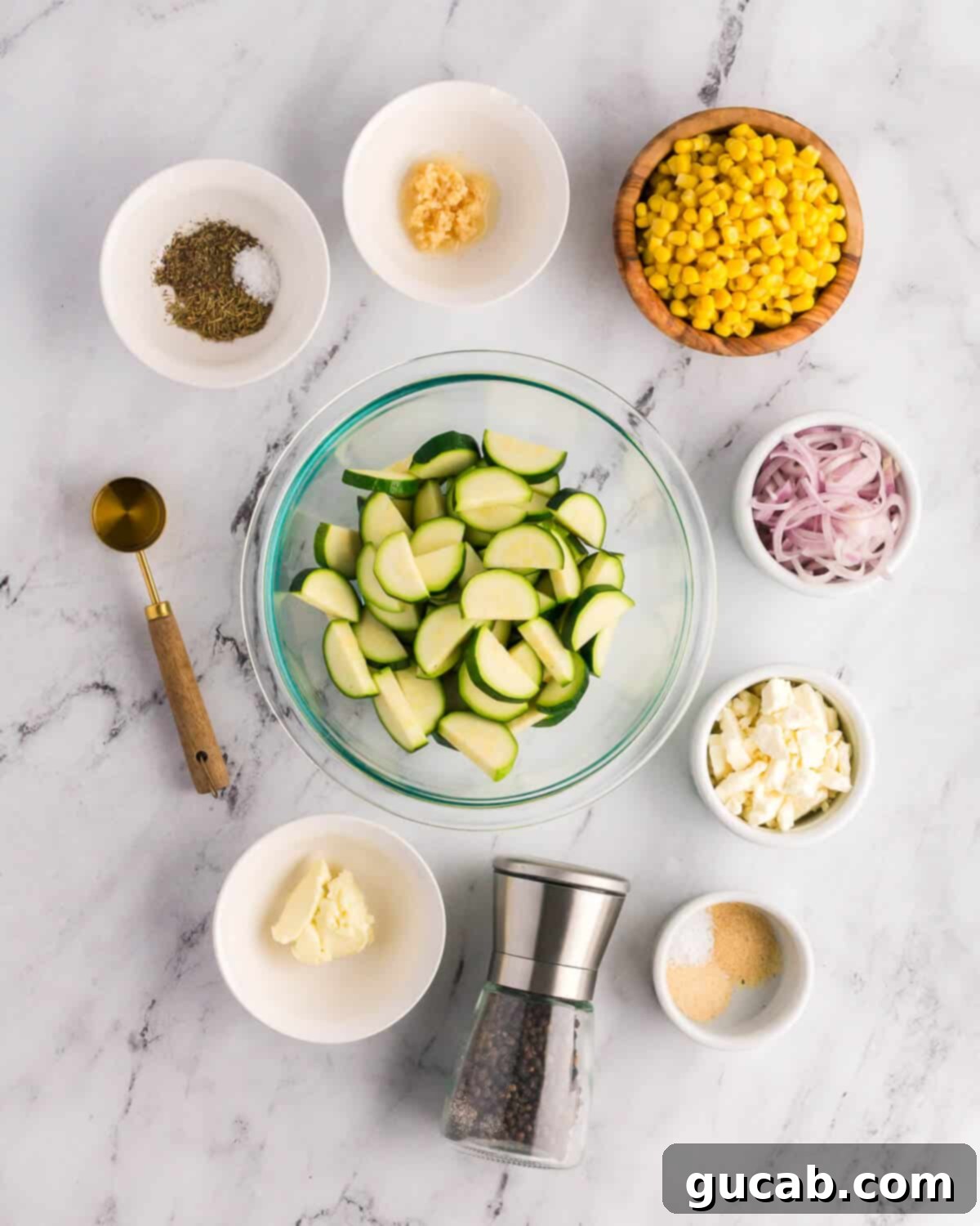 A flat lay image showing all the key ingredients: fresh garlic, sweet corn kernels, sliced shallots, vibrant zucchini, crumbled feta, a selection of spices, butter, and olive oil.