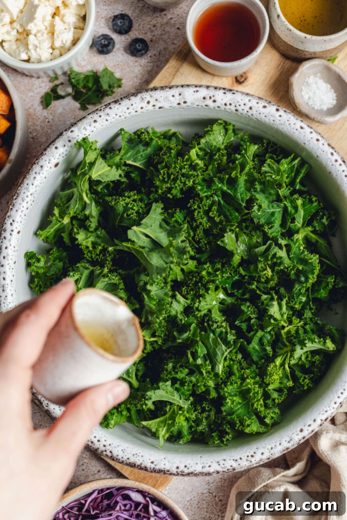 pouring olive oil onto a bowl of torn kale leaves.