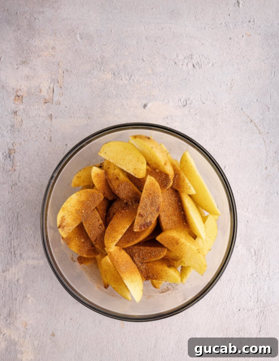 A bowl of cut and dried potato wedges, with taco seasoning sprinkled generously on top, ready for tossing.