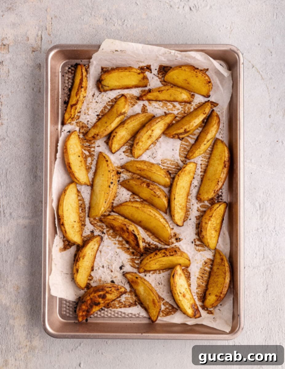 Golden-brown, roasted potato wedges scattered on a sheet pan, perfectly crispy and ready to be served.