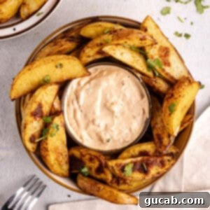 Crispy oven baked potato wedges surrounding a bowl of homemade chipotle sauce.