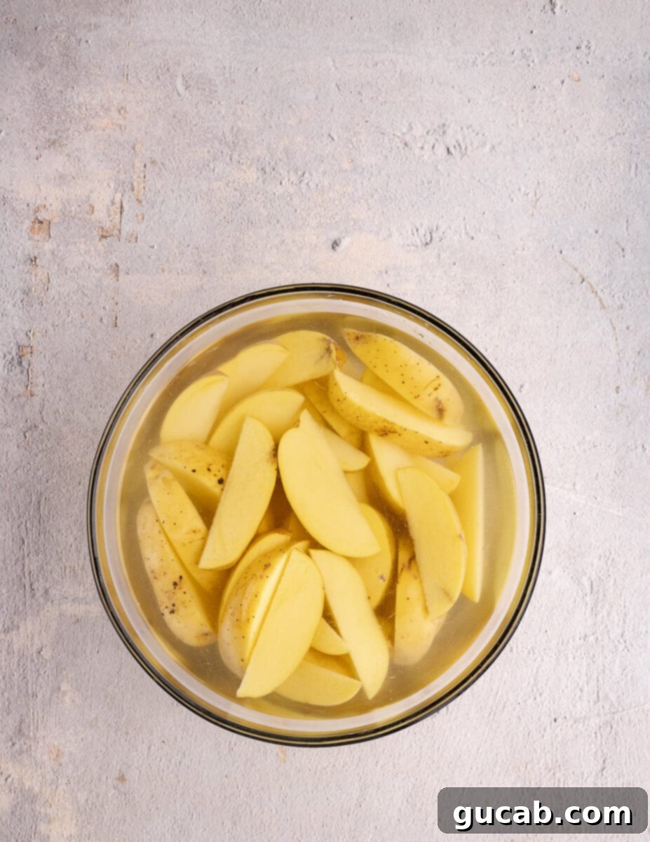 Gold potato wedges submerged in cold water within a bowl, illustrating the soaking process for crispier results.