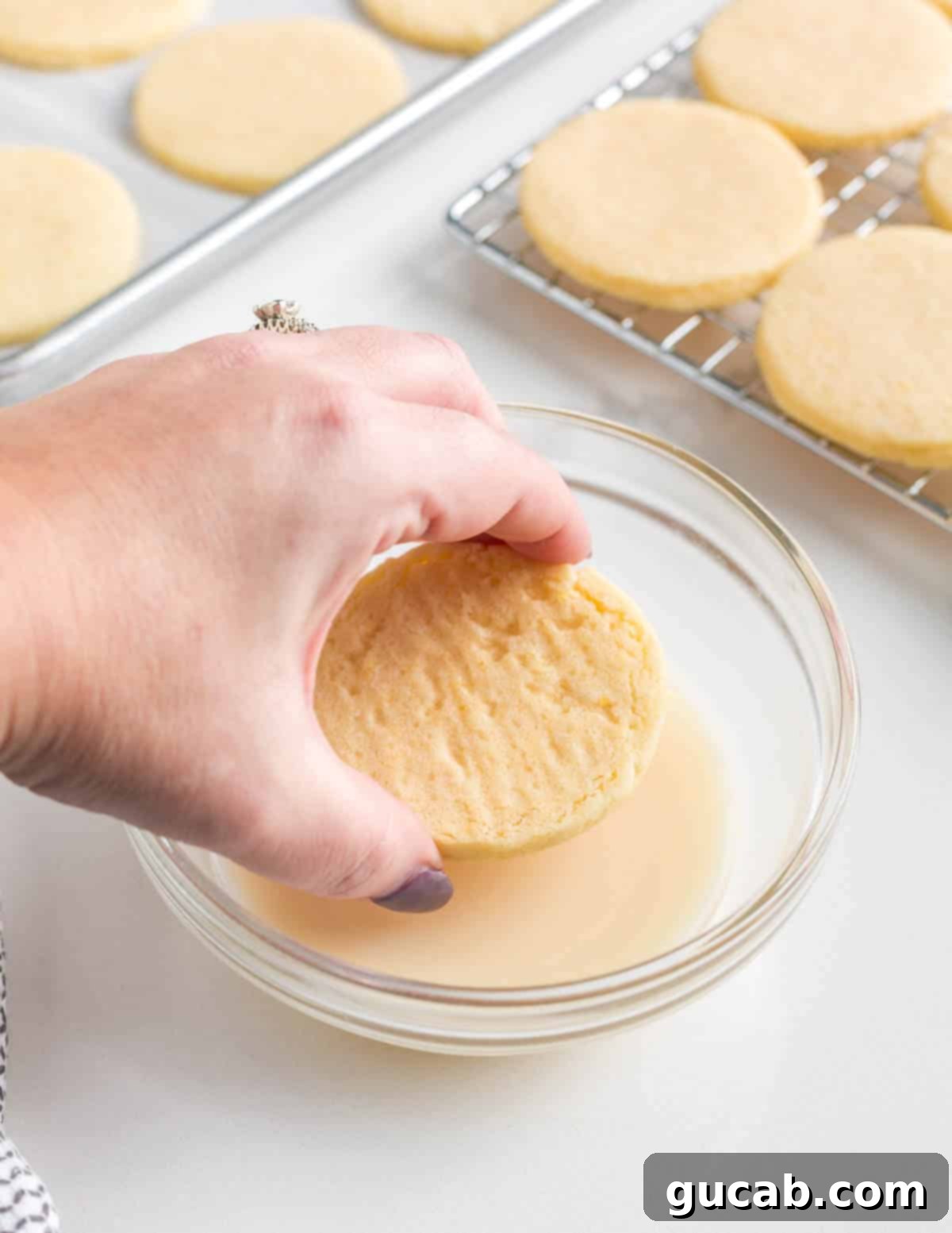 Sweet and Zesty Lemon Cookies 12 hand dipping a lemon cookie into lemon glaze.