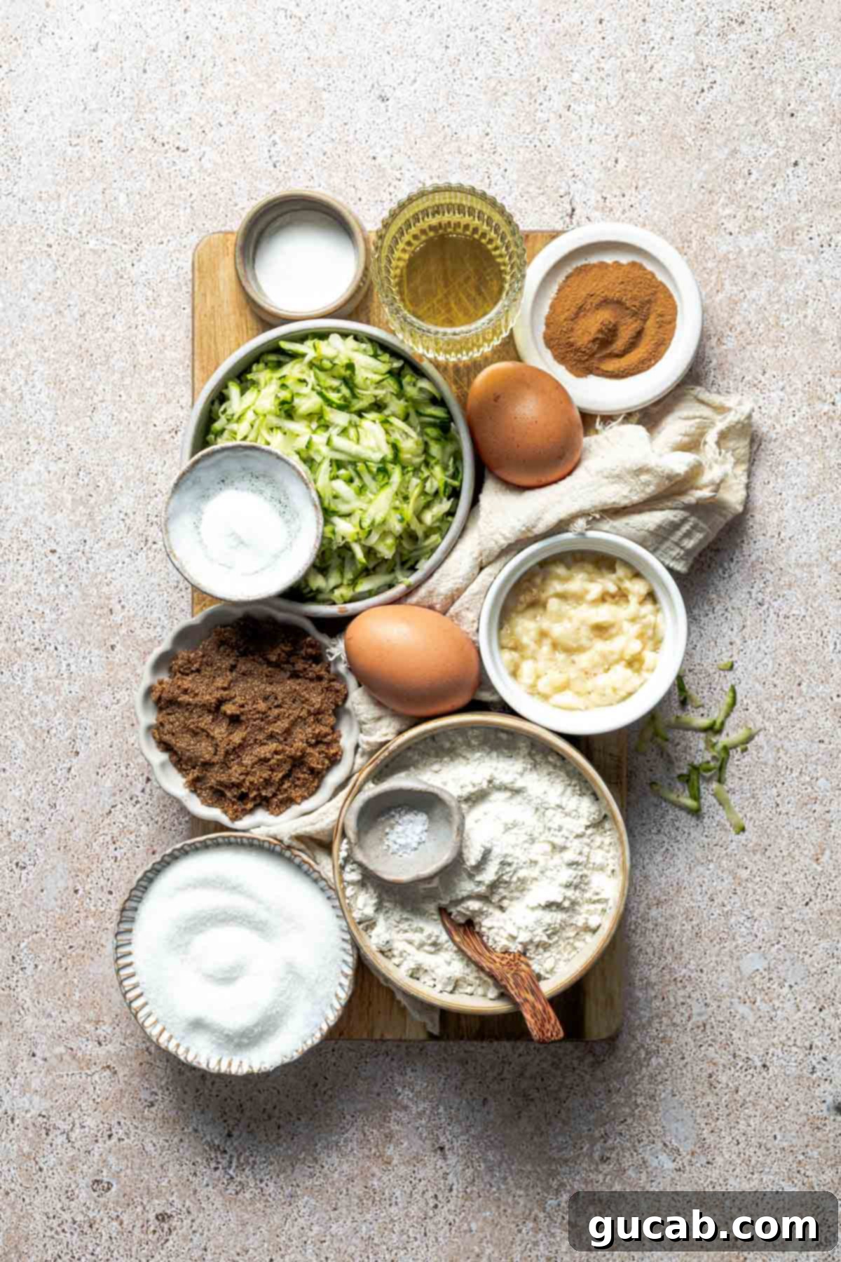 A vibrant selection of ingredients laid out, including vegetable oil, freshly grated zucchini, cinnamon sticks, brown eggs, mashed banana, both brown and white sugars, a bag of gluten-free all-purpose flour, and a small pinch of salt, all essential for making this delicious gluten-free zucchini bread.