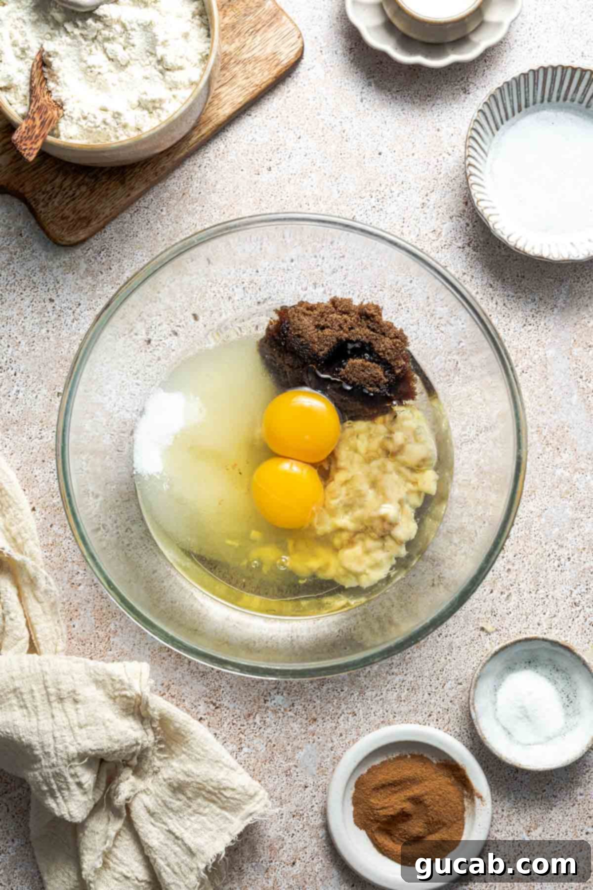A large mixing bowl containing mashed banana, eggs, white sugar, dark brown sugar, and vegetable oil, before mixing.