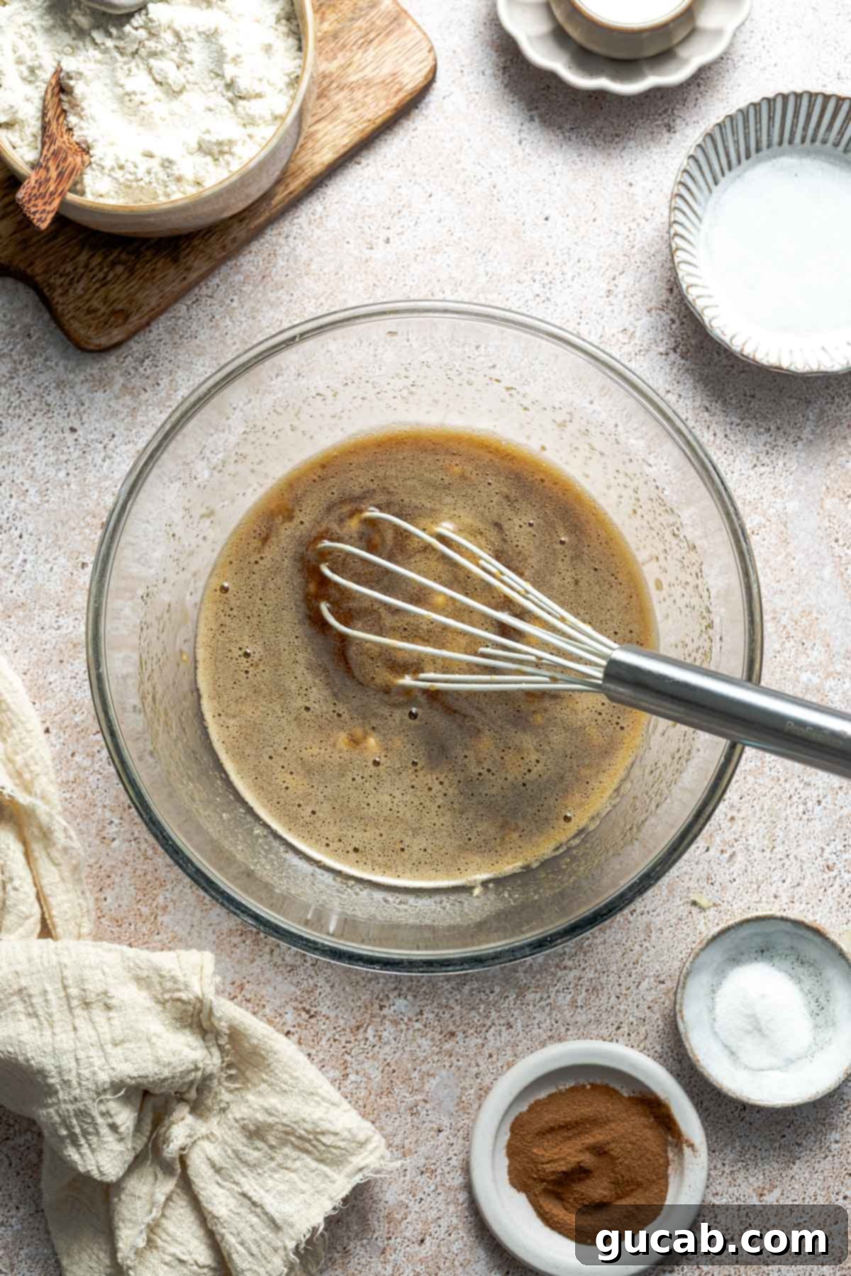 The smoothly whisked mixture of sugar, mashed banana, and eggs in a bowl, showing a uniform and light consistency before dry ingredients are added.