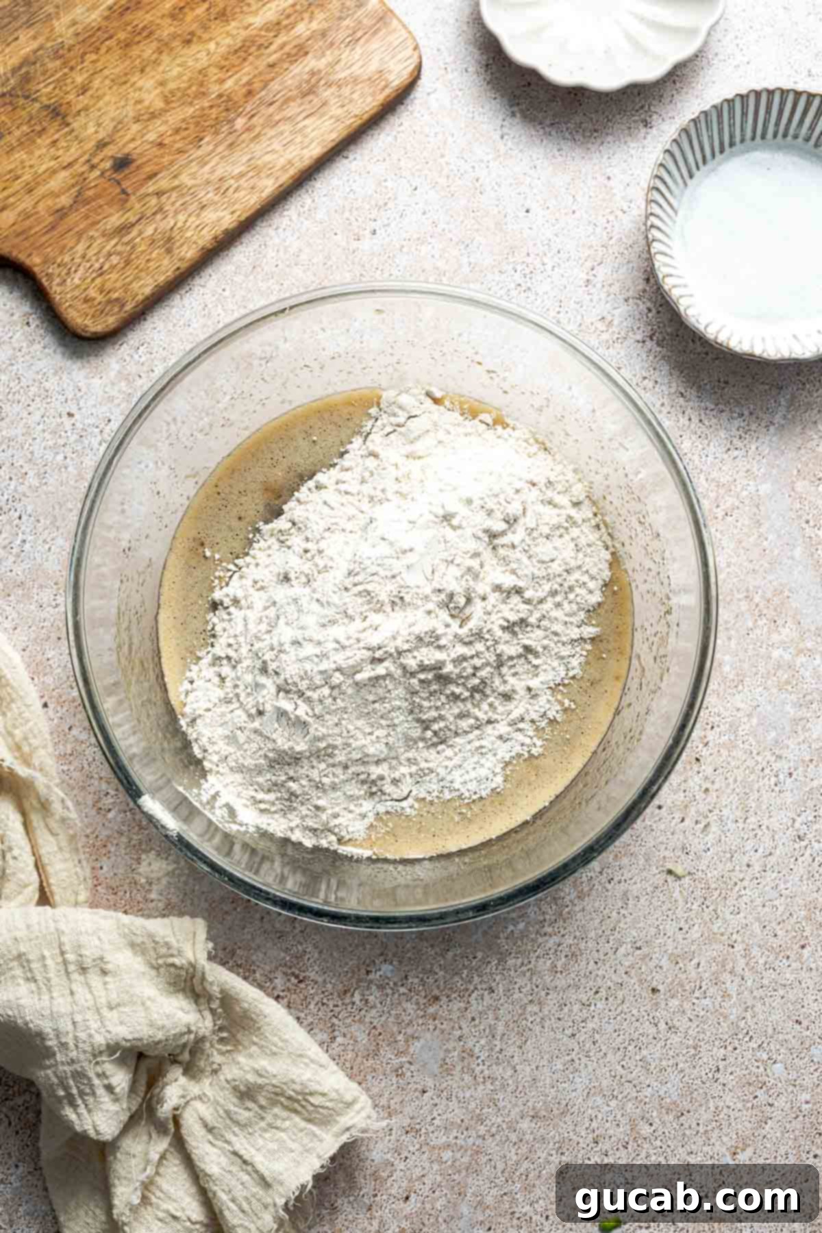 All-purpose gluten-free flour, baking powder, baking soda, cinnamon, and salt resting on top of the whisked wet ingredients in a bowl, ready to be mixed into the batter.