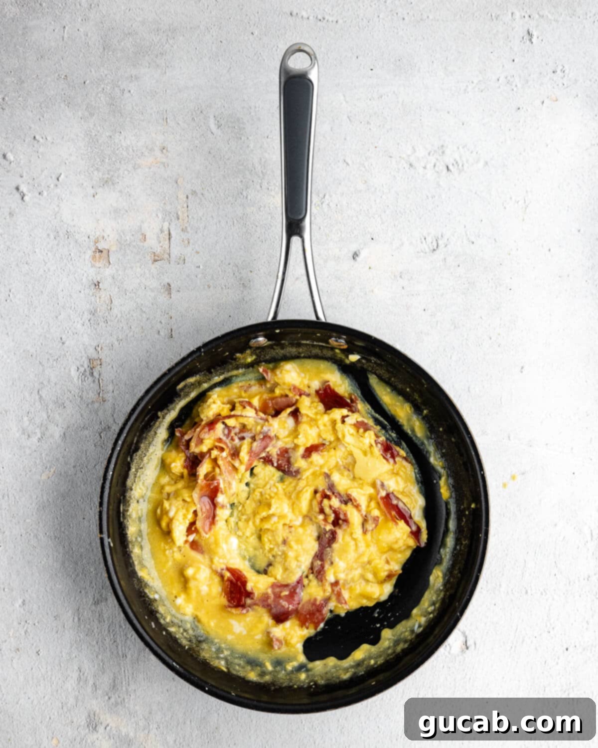 Savory Prosciutto & Cheese Scramble 11 Scrambled eggs mixed with crispy prosciutto in a skillet, still cooking to a soft consistency.