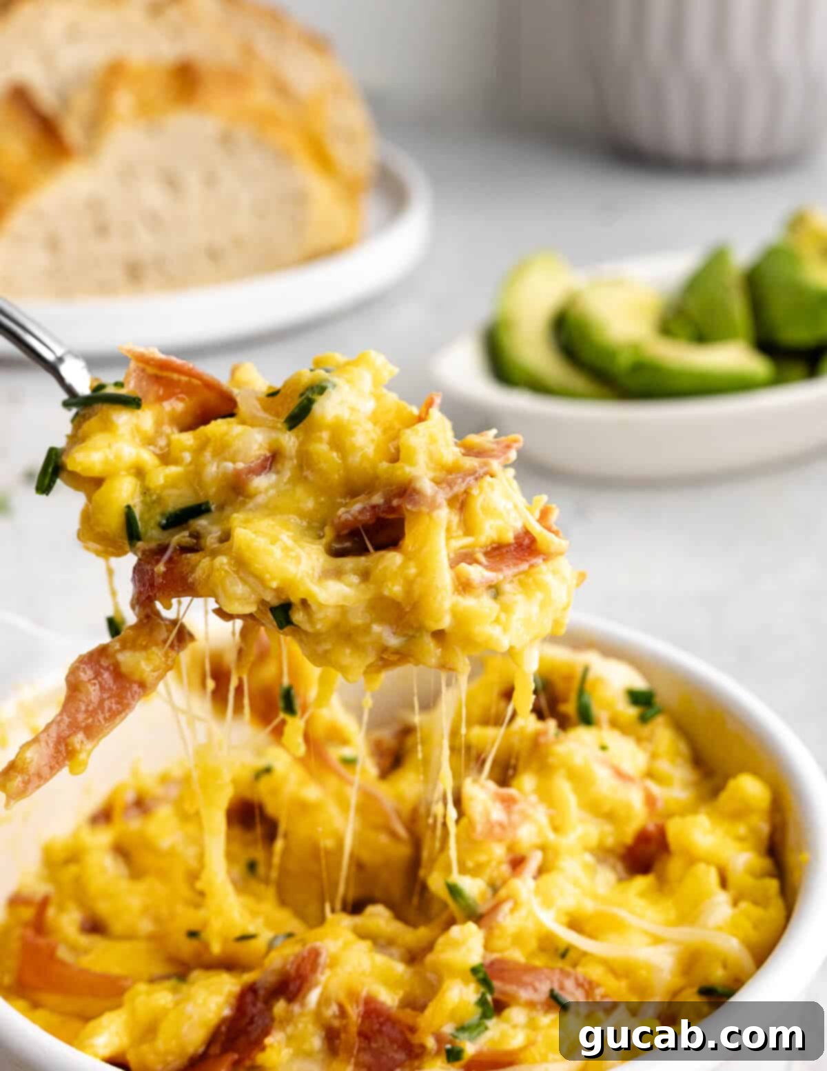 Savory Prosciutto & Cheese Scramble 4 a large bite of fluffy cheesy eggs with crispy prosciutto and fresh chives on a fork, showing the texture and ingredients