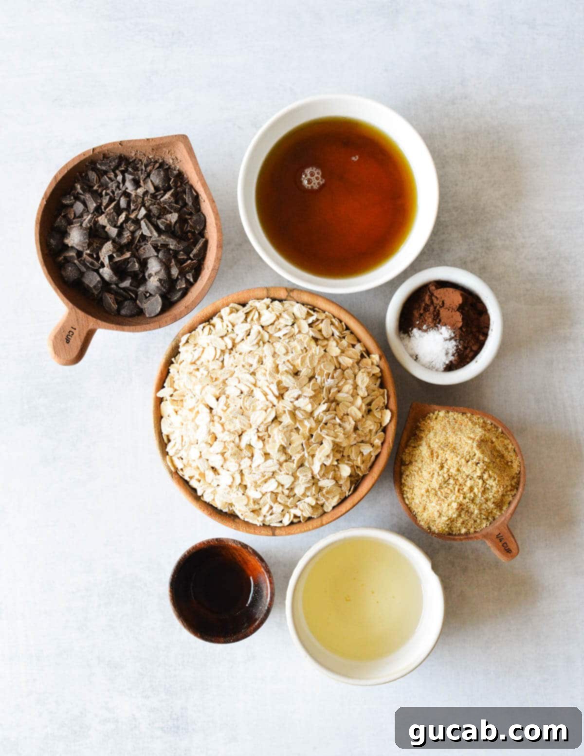 Dark Chocolate Granola 3 A rustic spread of key ingredients including maple syrup, chunks of dark chocolate, old-fashioned oats, golden flax meal, cocoa powder, a pinch of salt, melted coconut oil, and a bottle of vanilla extract.