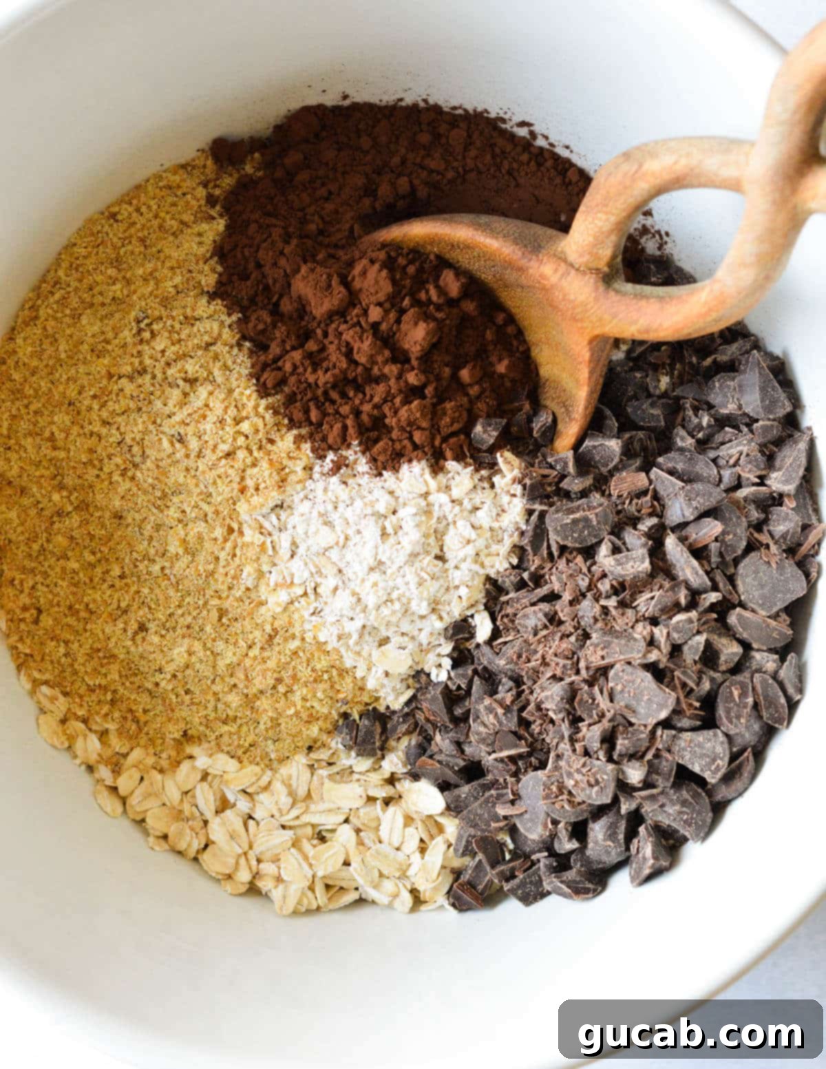 Dark Chocolate Granola 7 A large bowl containing a mixture of dry ingredients: whole oats, ground oats, golden flax meal, cocoa powder, finely chopped dark chocolate, and a sprinkle of salt.