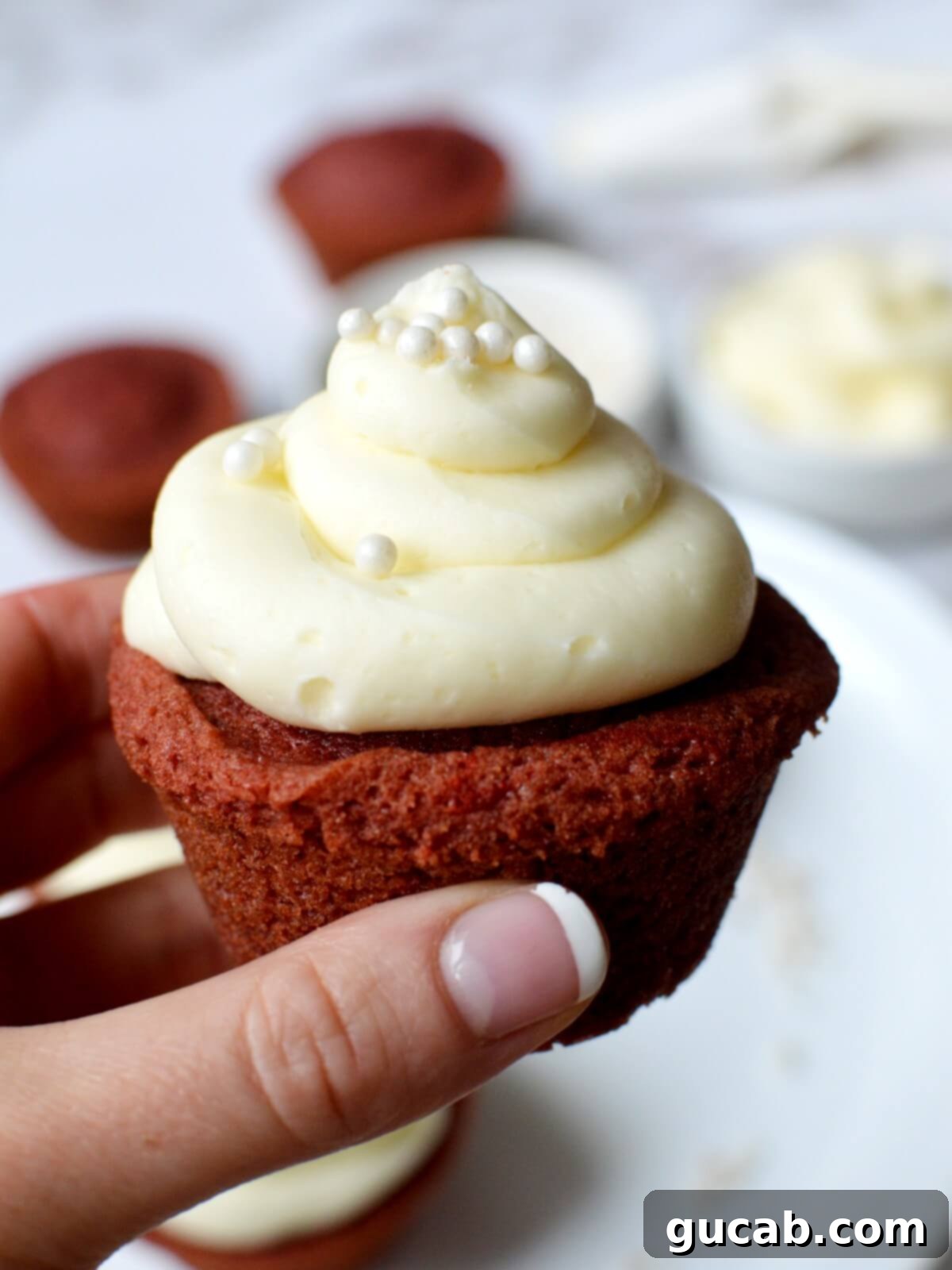 A hand presenting a beautifully frosted gluten-free red velvet cupcake, a classic Easter treat.