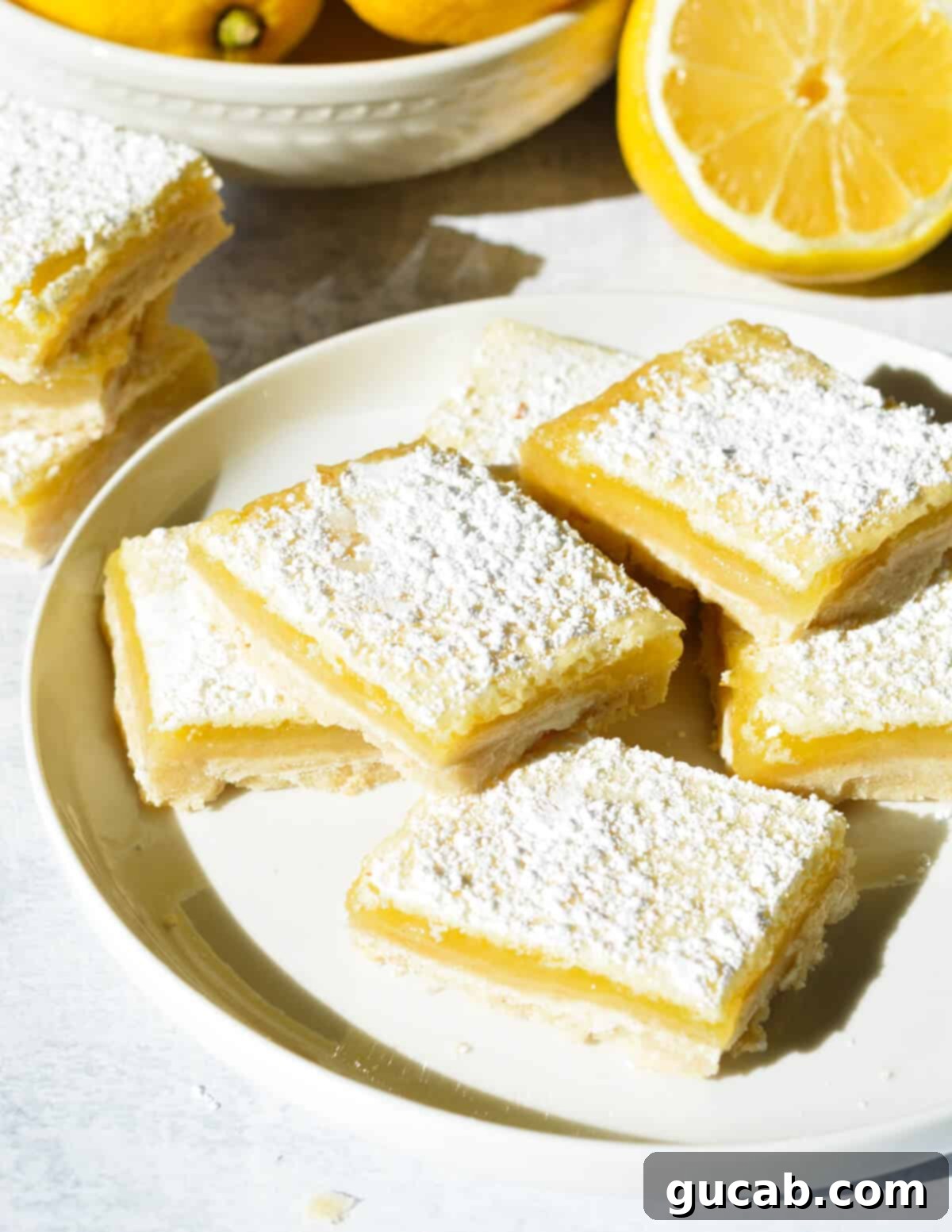 A plate stacked with perfectly square gluten-free lemon bars, glistening with a dusting of powdered sugar.