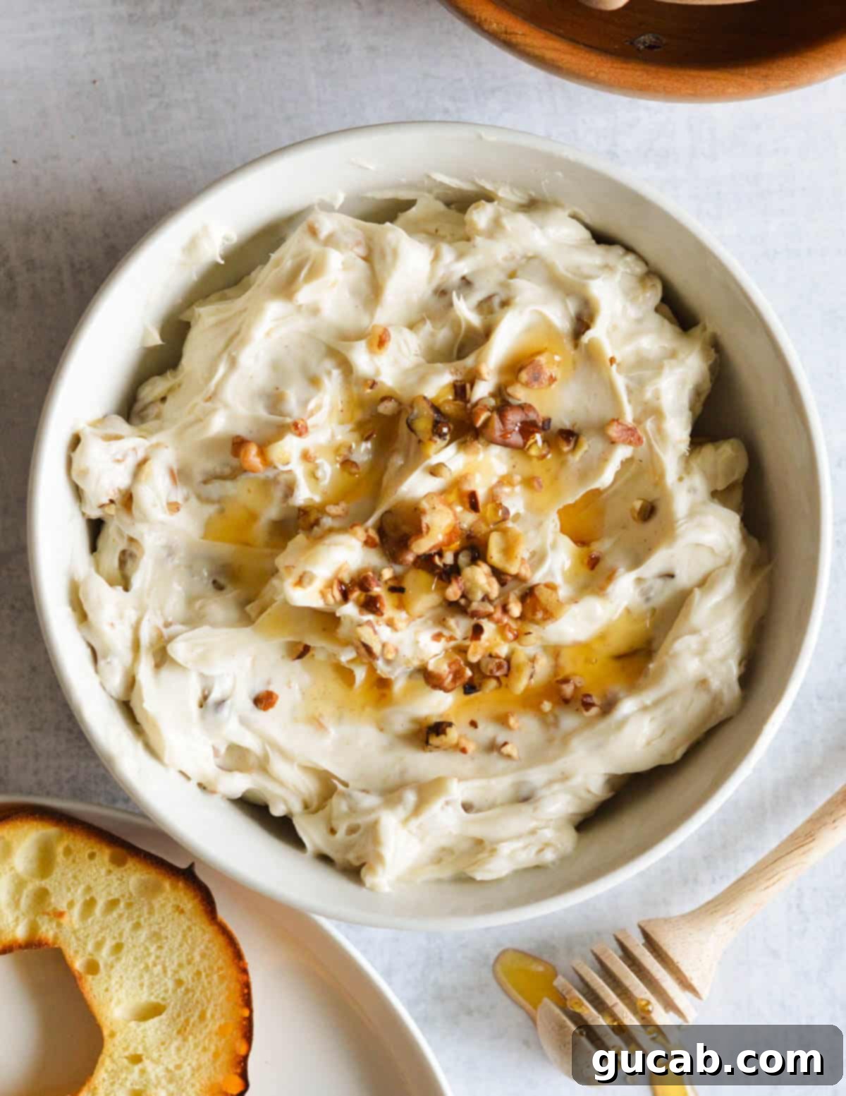 A bowl of homemade honey walnut cream cheese, garnished with chopped walnuts and a drizzle of golden honey on top, ready to be served.