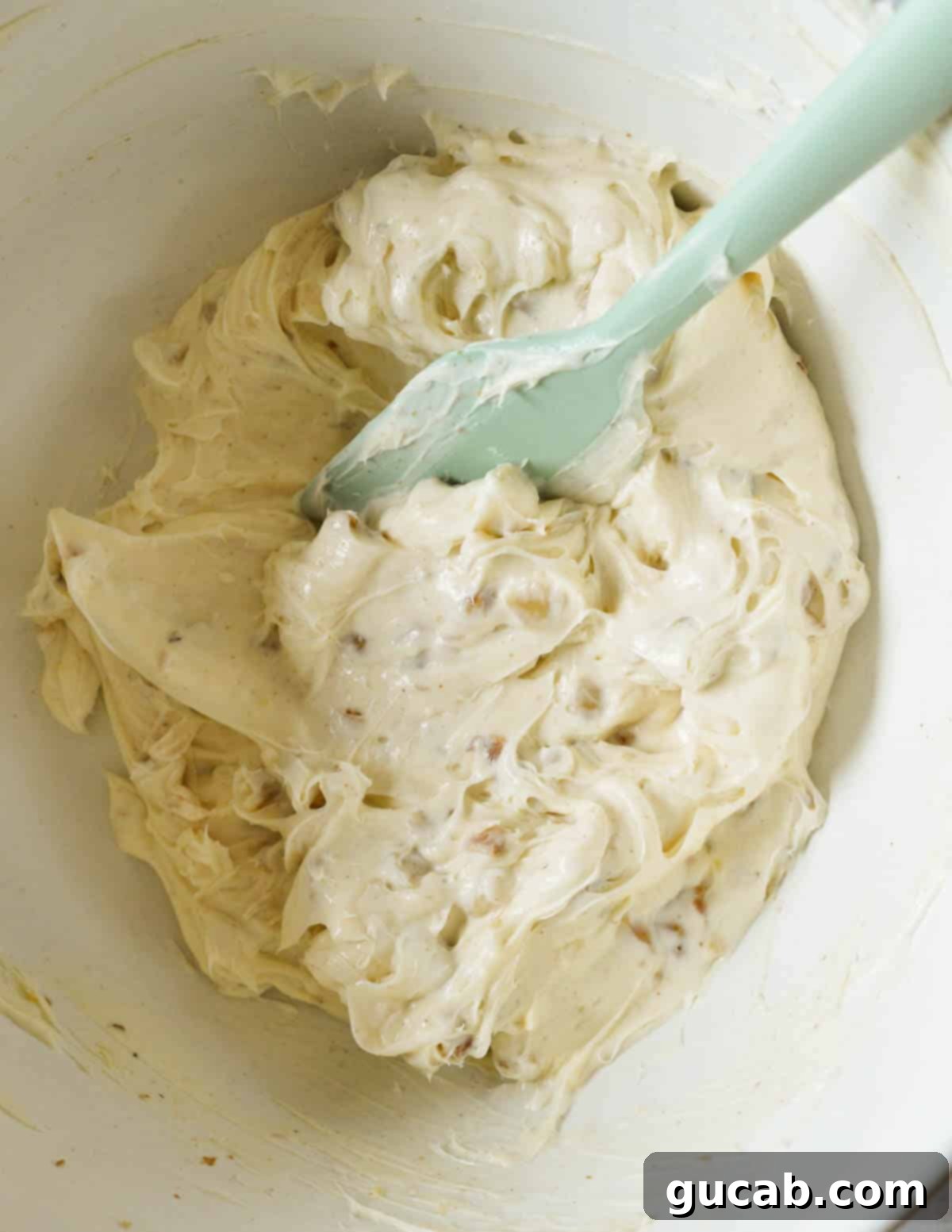 A large bowl filled with the finished honey walnut cream cheese, showing its creamy texture and evenly distributed walnut pieces, with a spatula resting in it.