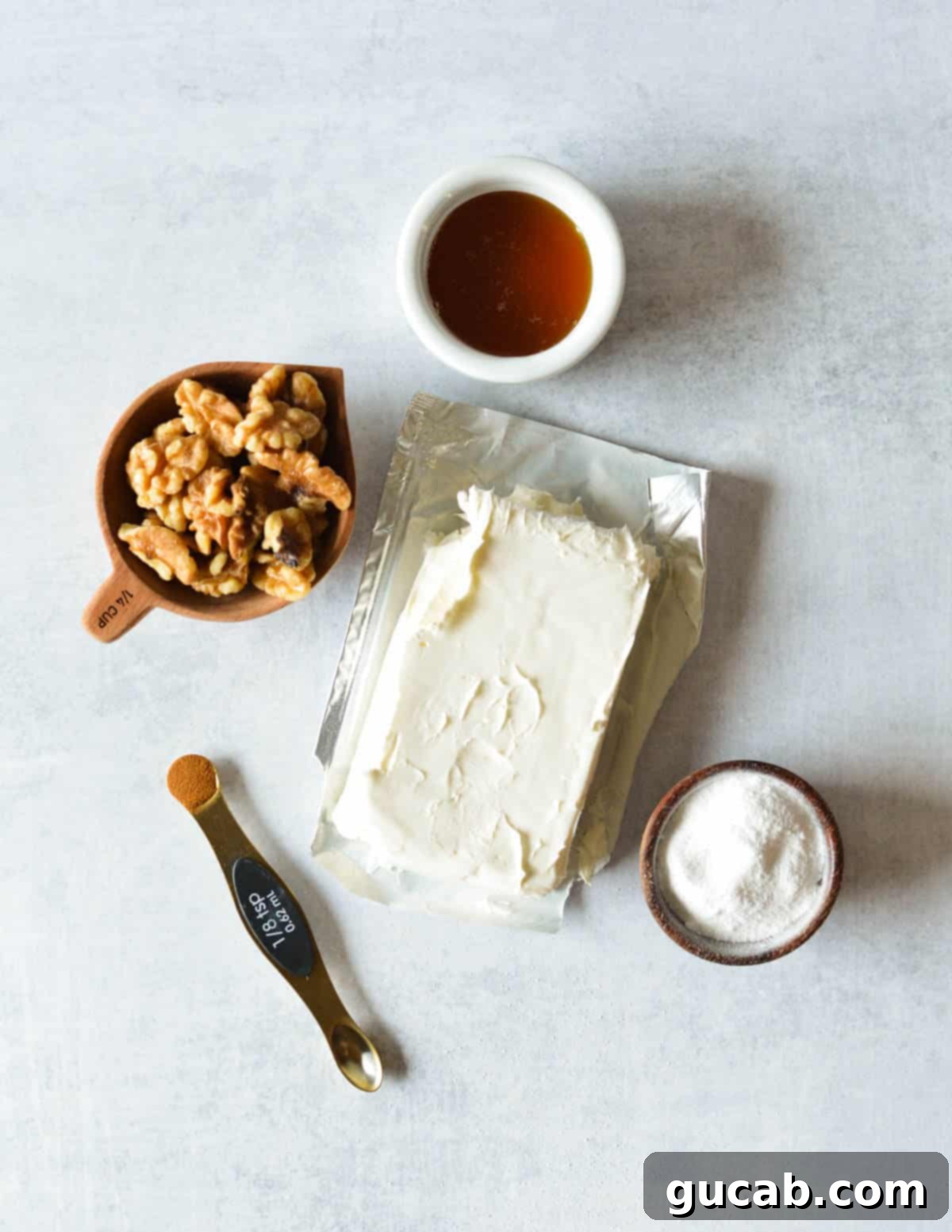Key ingredients for honey walnut cream cheese laid out: honey, a block of cream cheese, raw walnuts, cinnamon powder, and powdered sugar.