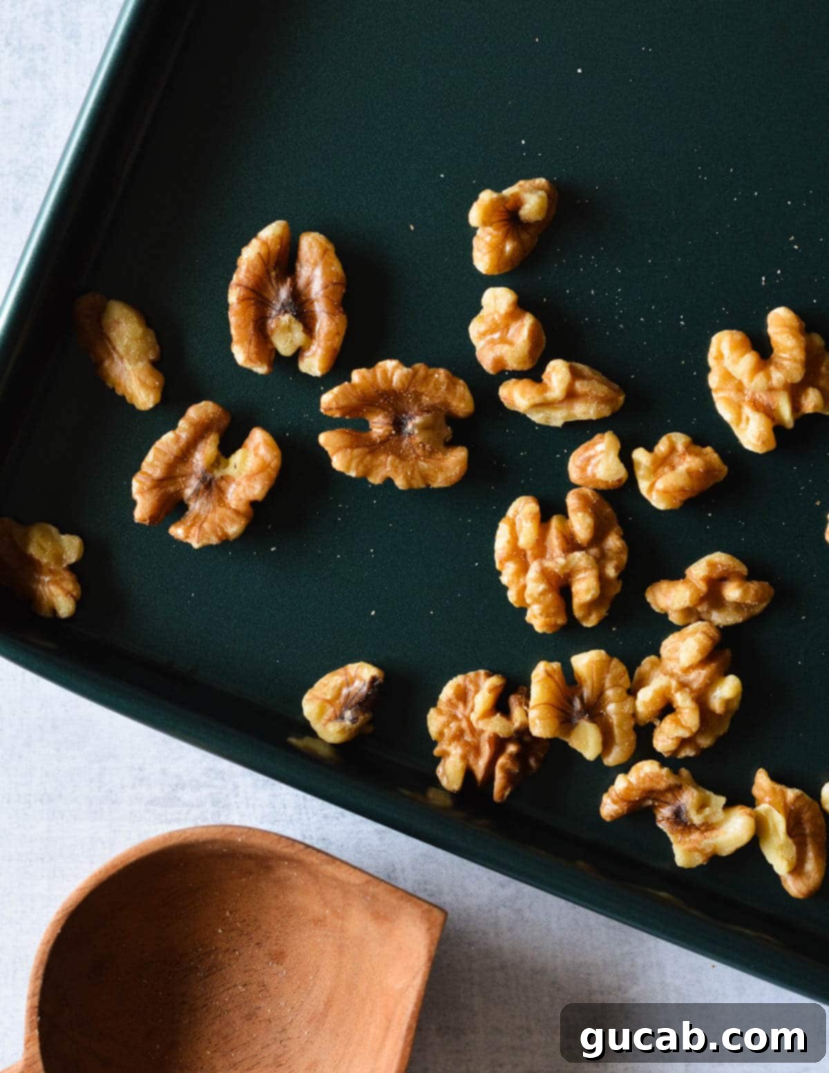 Golden brown, toasted walnuts are shown on a baking sheet after being removed from the oven, fragrant and slightly darker.