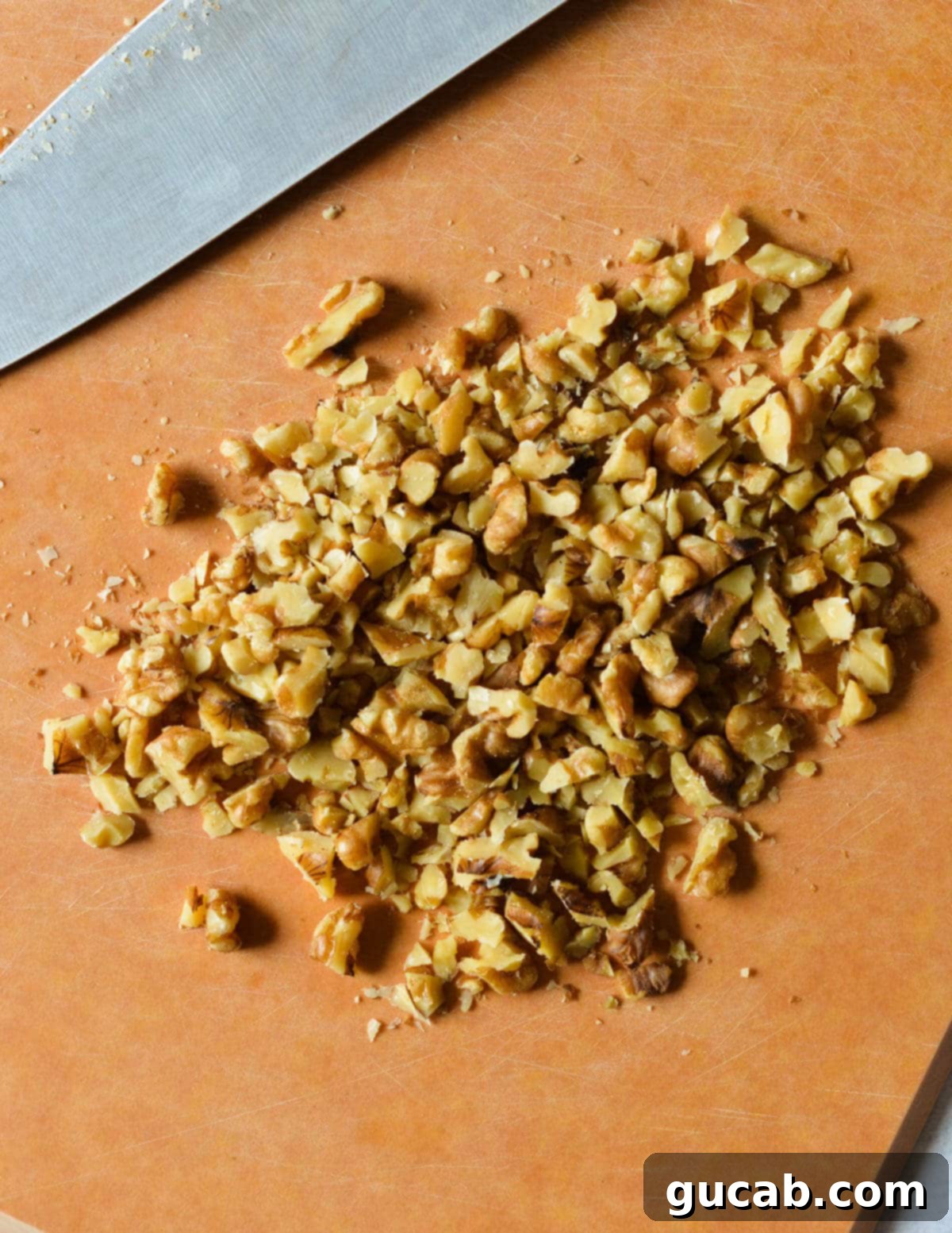 Finely chopped walnuts are neatly arranged on a cutting board, ready to be incorporated into the cream cheese.