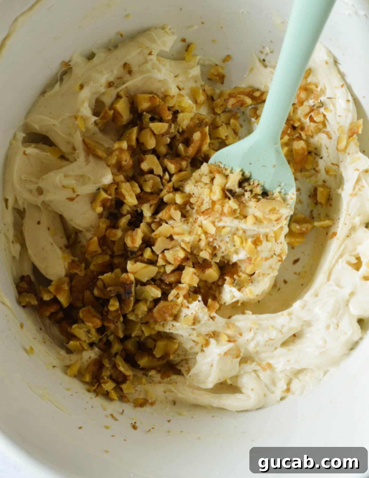 Finely chopped walnuts are being added to the whipped honey cream cheese mixture in a bowl.