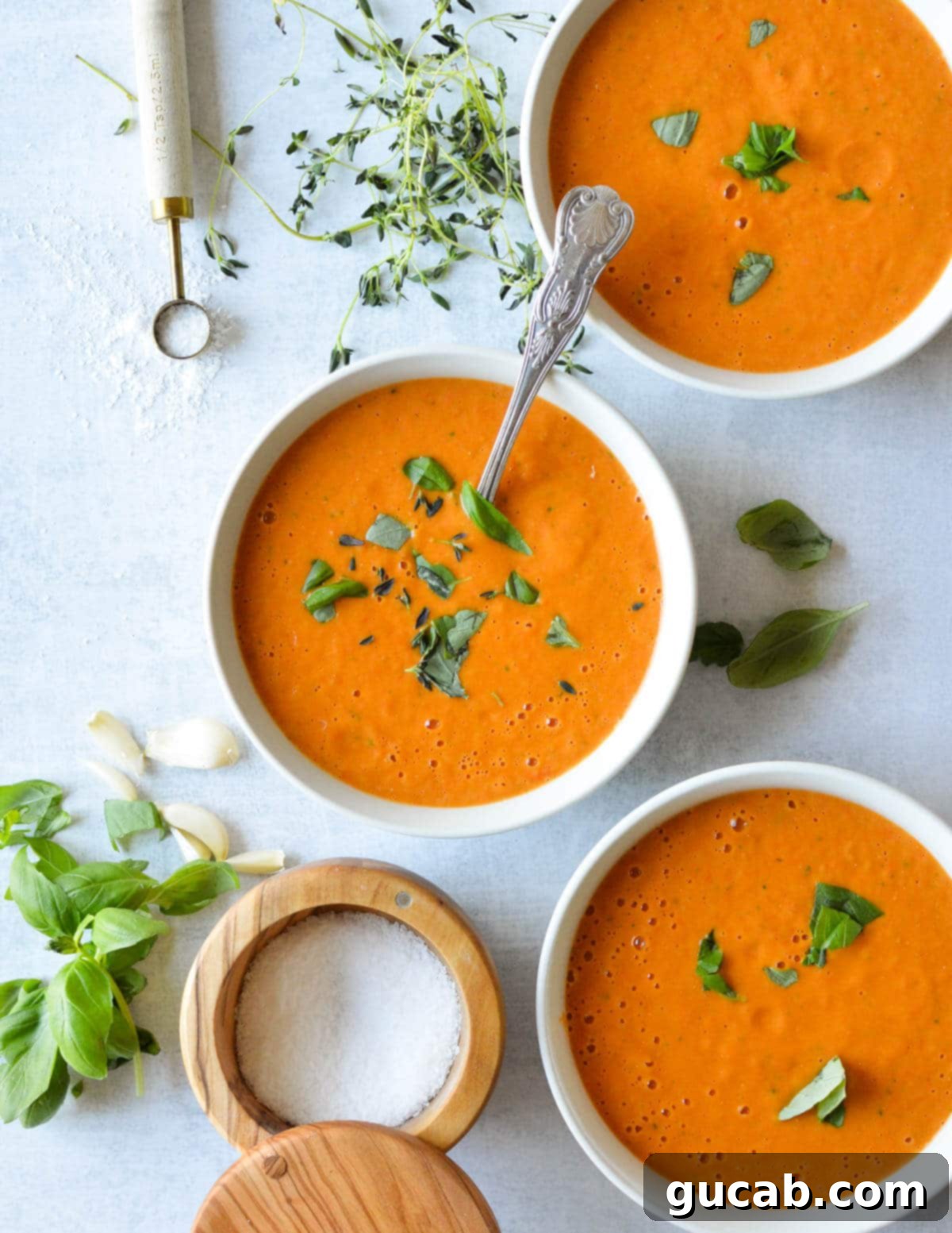 Cherry Tomato Soup 2 Three elegant bowls of creamy roasted cherry tomato soup, each garnished with vibrant fresh basil leaves, suggesting a warm and inviting meal.