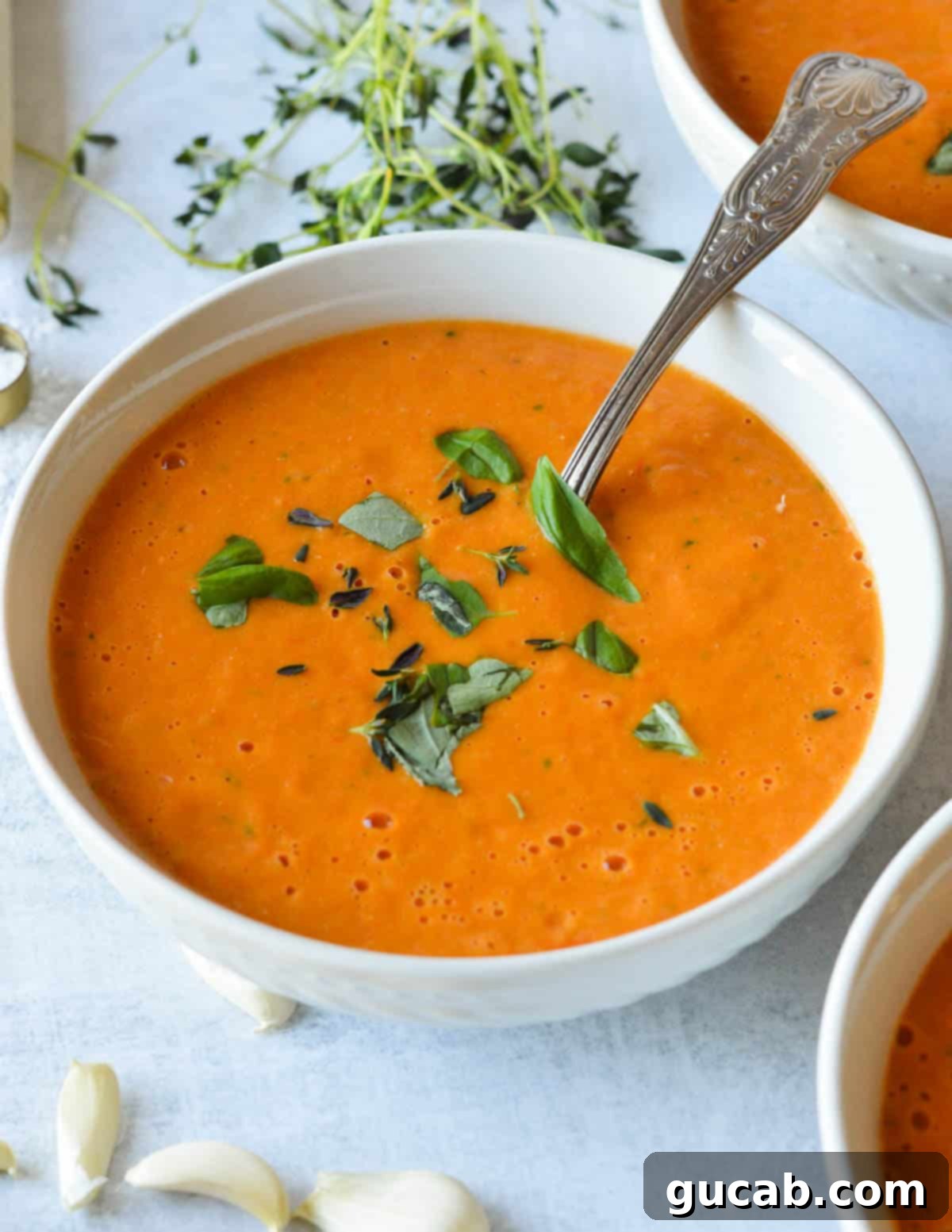 Cherry Tomato Soup 12 A beautifully presented, steaming bowl of creamy roasted cherry tomato soup, generously garnished with vibrant fresh basil leaves, ready to be enjoyed.