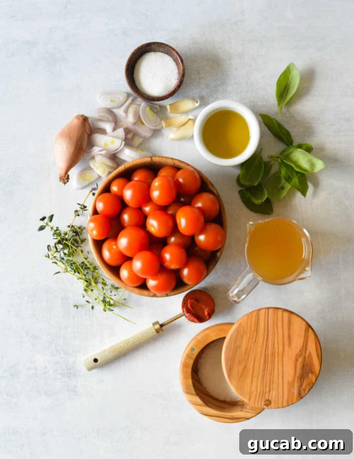 Cherry Tomato Soup 3 A collection of fresh ingredients laid out: granulated sugar, thinly sliced shallots, clear olive oil, vibrant fresh basil leaves, whole garlic cloves, vegetable stock in a measuring cup, sprigs of fresh thyme, kosher salt, and rich tomato paste.