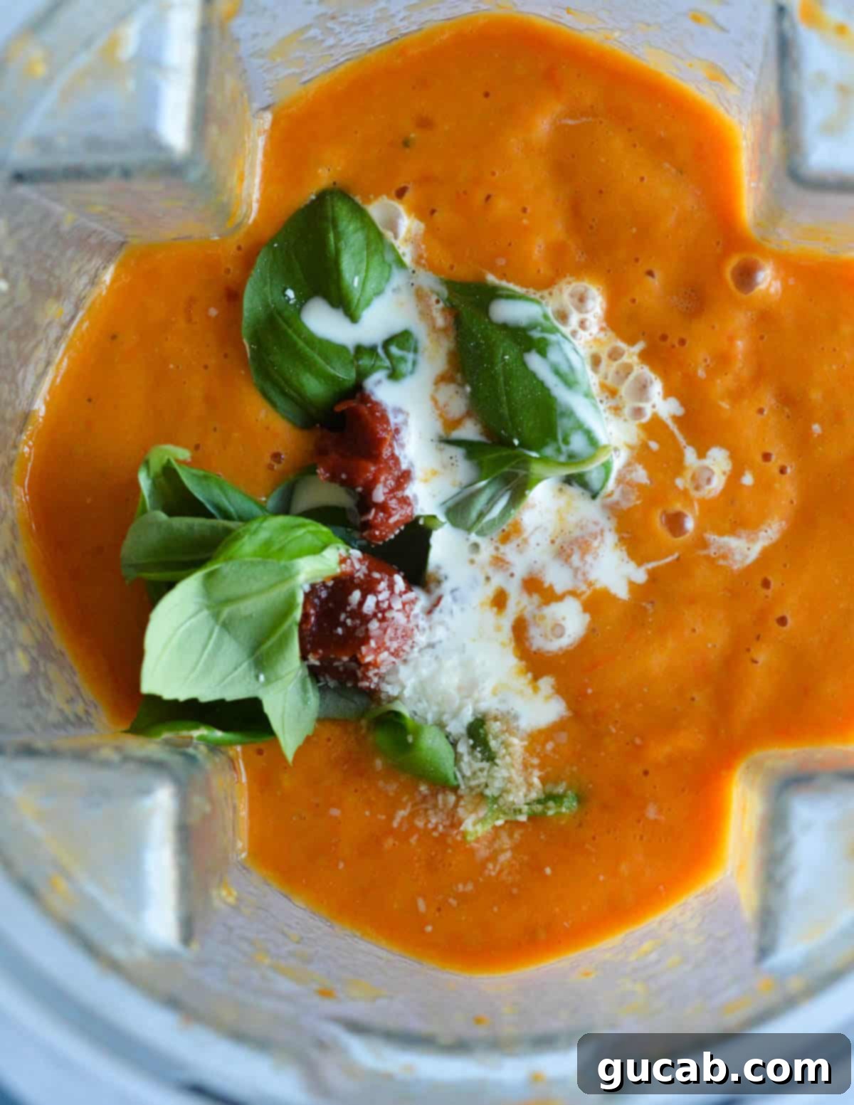 Cherry Tomato Soup 9 Smooth, blended tomato soup in a blender, with vibrant fresh basil, rich heavy cream, and concentrated tomato paste added on top, ready for the final blend.