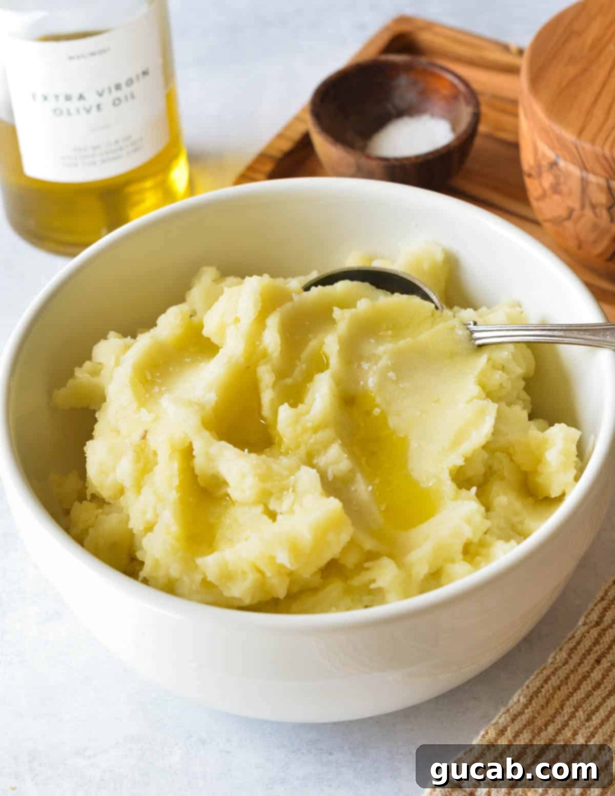 A bowl of irresistibly creamy olive oil mashed potatoes, garnished with a drizzle of olive oil and fresh herbs.