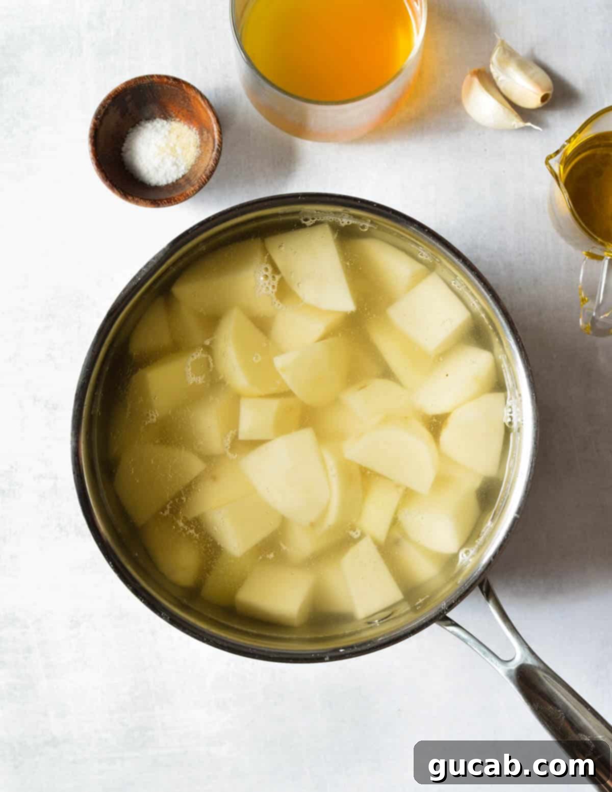 Cut russet potato chunks submerged in cold water in a pot on the stovetop, just before boiling.
