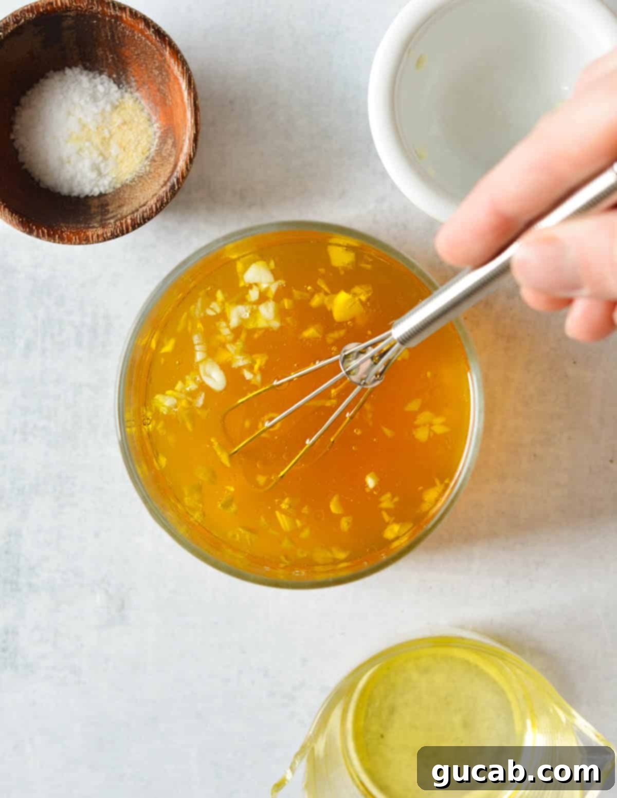 Vegetable stock, olive oil, and minced garlic mixed together in a clear liquid measuring cup, ready to be warmed.
