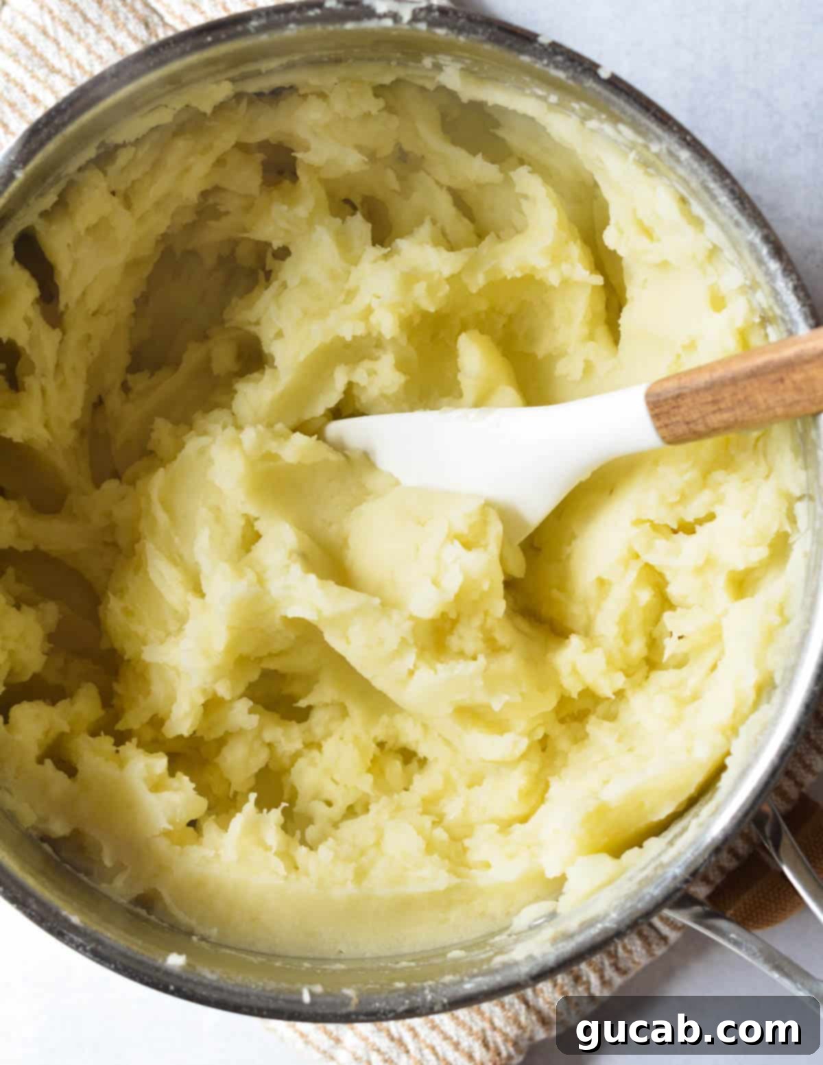 A top-down shot of perfectly smooth and creamy mashed potatoes in a pot, ready to be served.