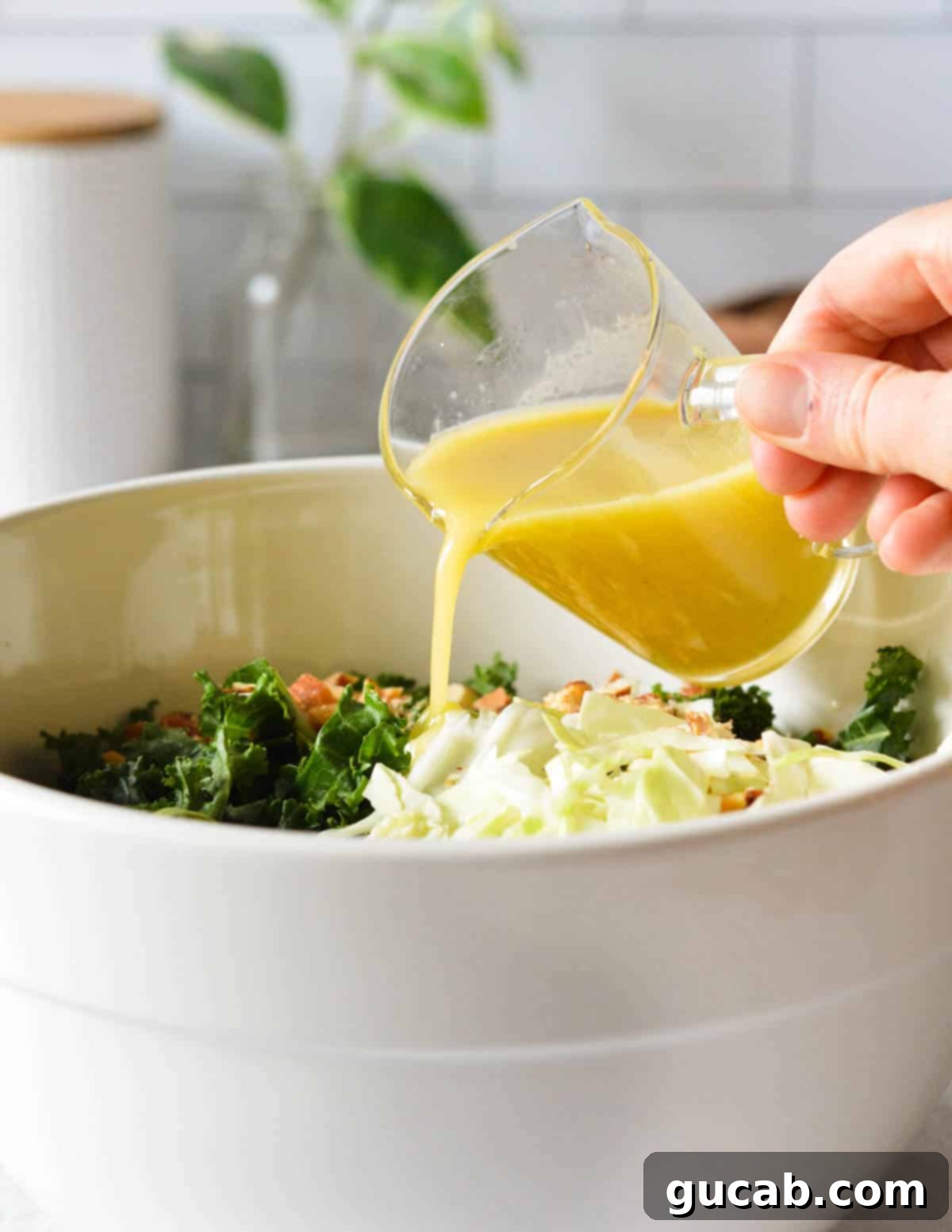 Kale Crunch Salad 11 hand pouring an apple dijon vinaigrette onto a kale salad.