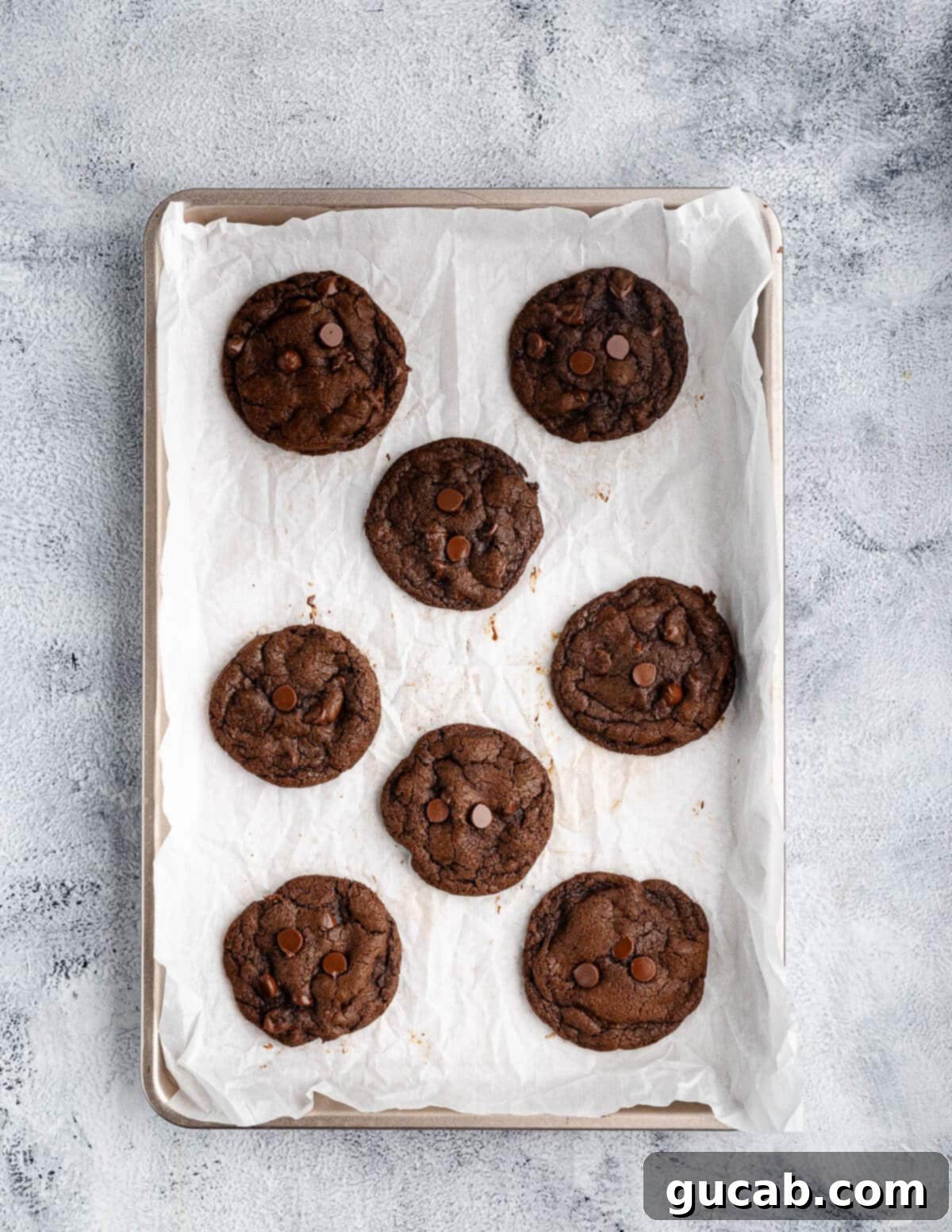 Freshly baked triple chocolate cookies cooling on a sheet pan, showcasing their rich color and soft texture.