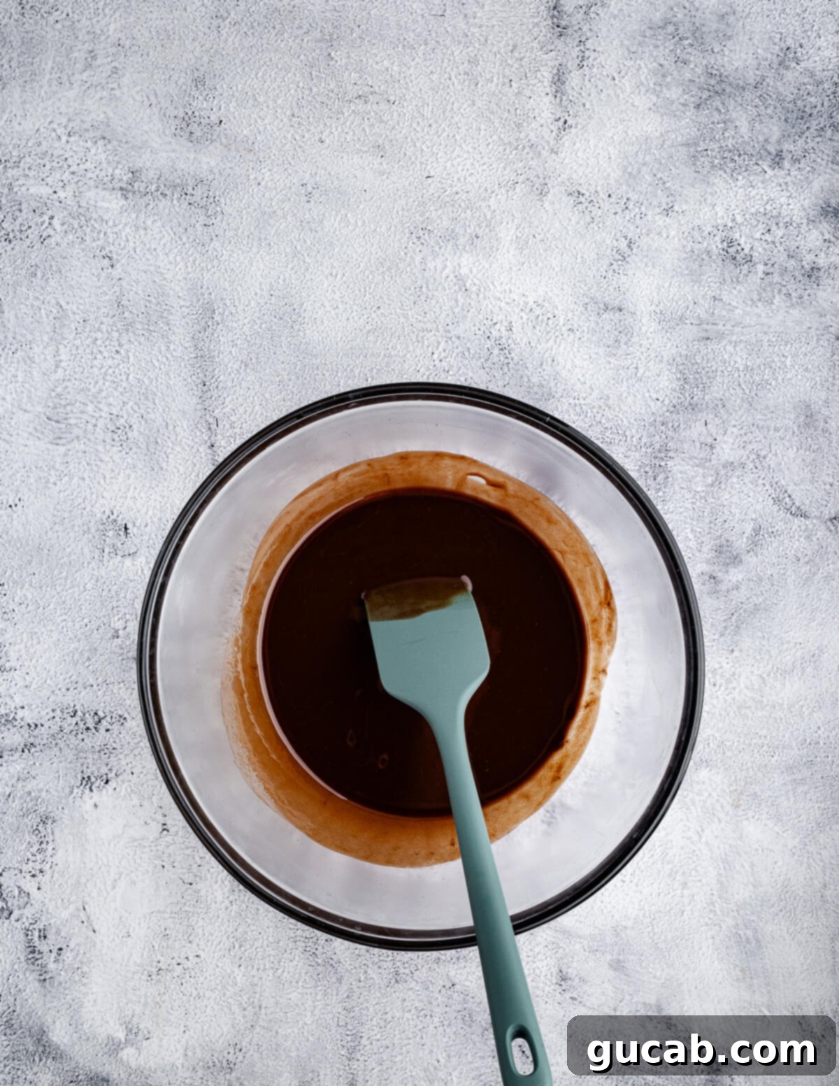 A spatula stirring the melted chocolate and butter mixture in a bowl, ensuring smooth consistency.
