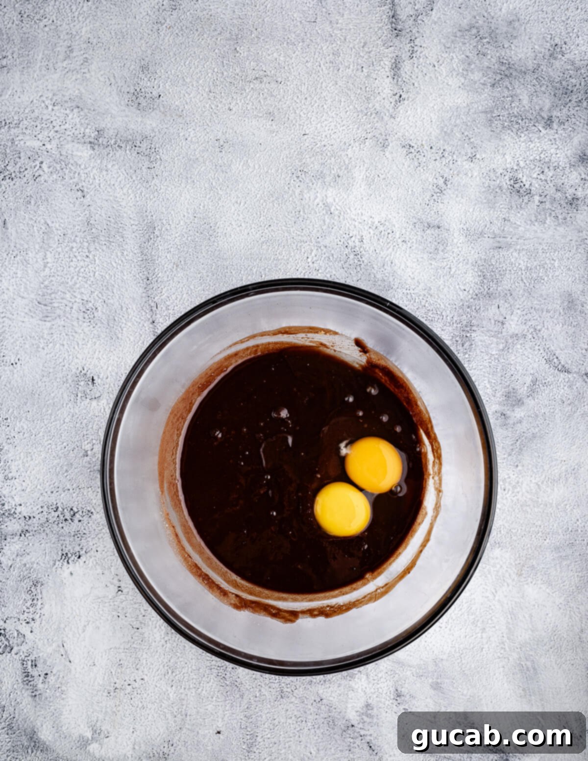 A bowl of melted chocolate mixture with a whole egg and an egg yolk freshly added.