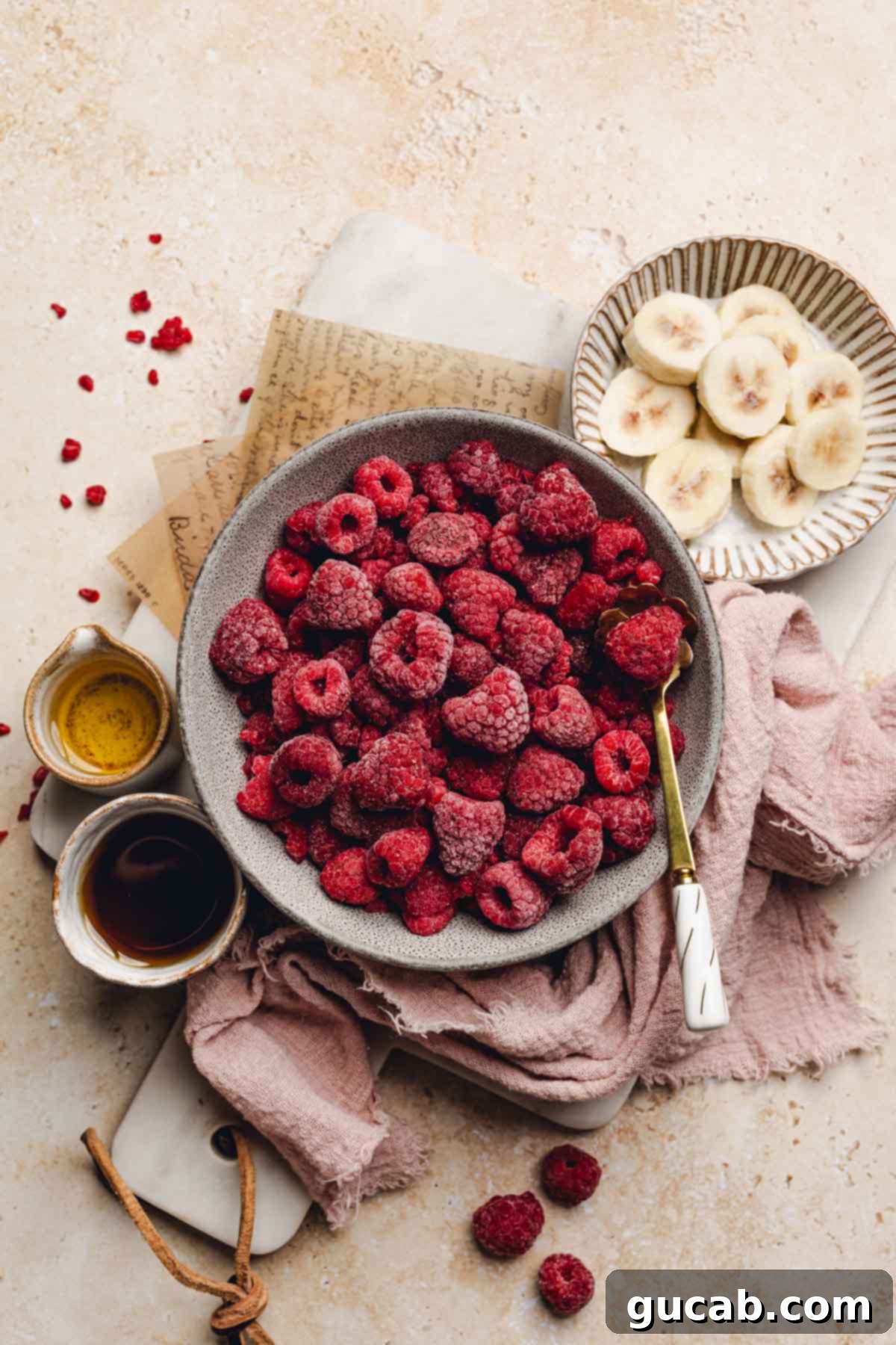 A flat lay image showing the key ingredients: frozen banana slices, frozen raspberries, maple syrup, and apple juice.